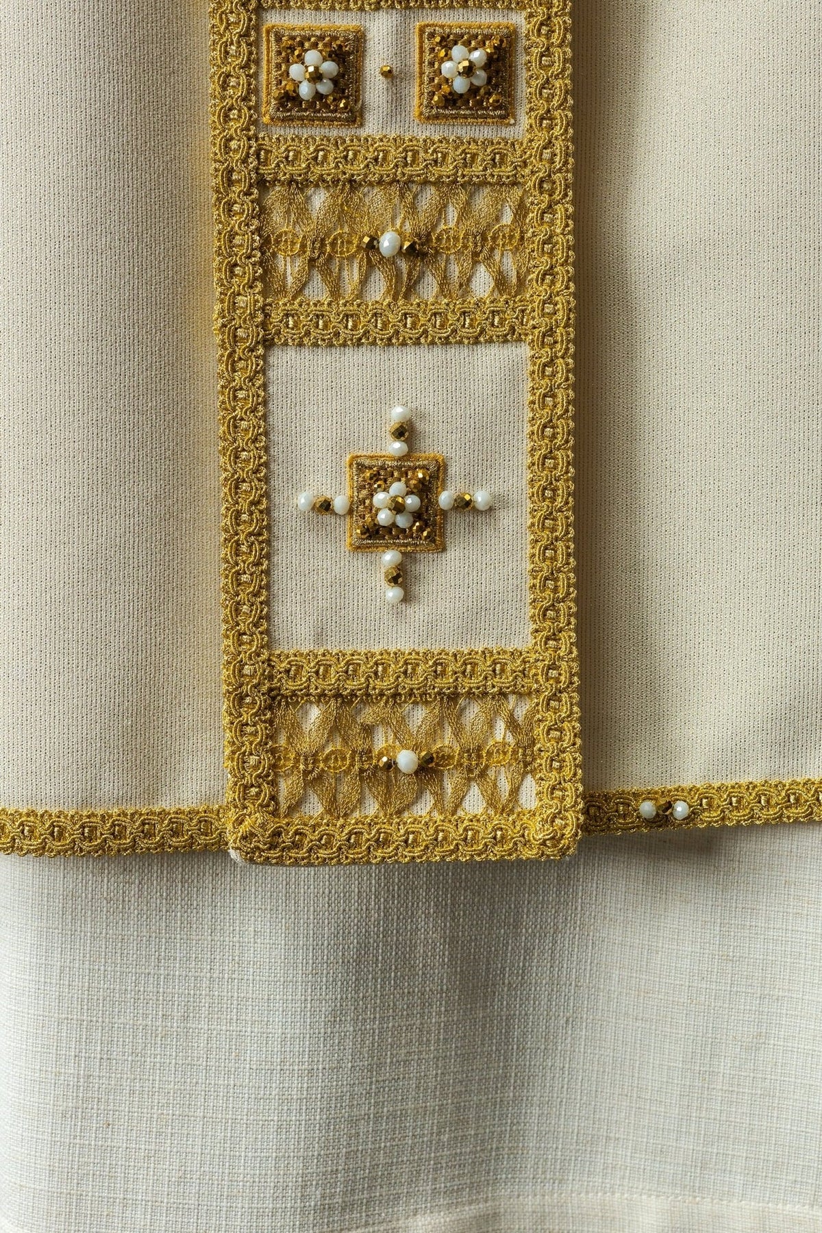 Chasuble orphrey close-up with gold embroidery, white stones and square motifs