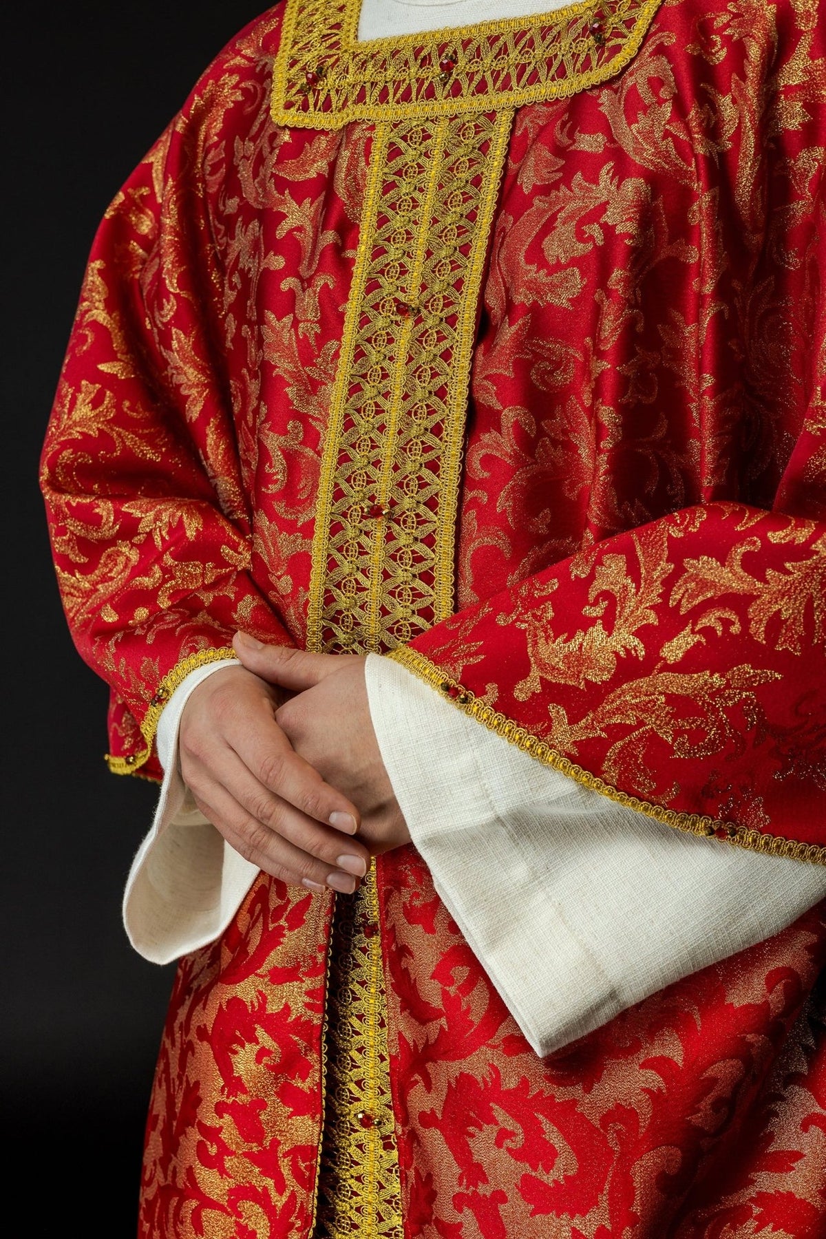Red and gold chasuble close-up showing ornate central orphrey and patterned fabric