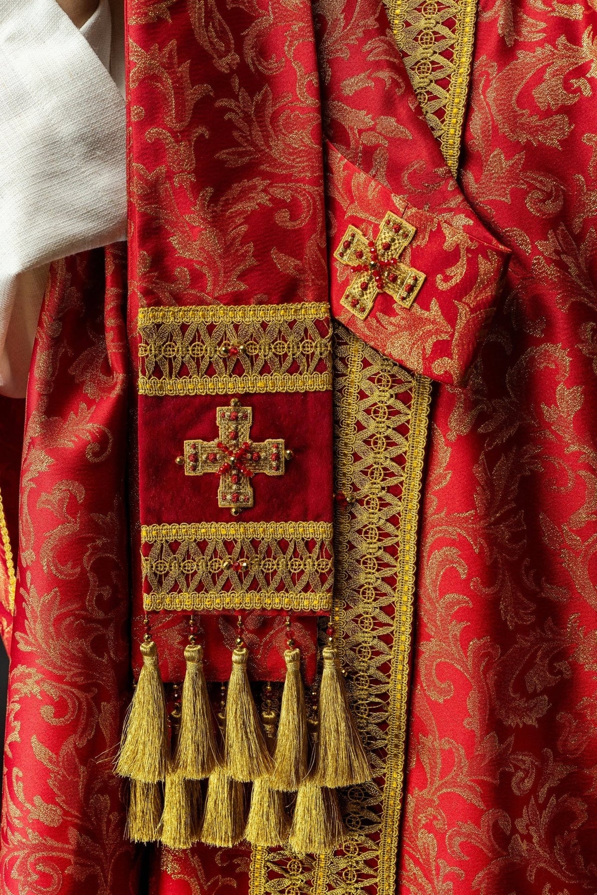 Red and gold chasuble detail showing cross embroidery, natural stones and gold tassel