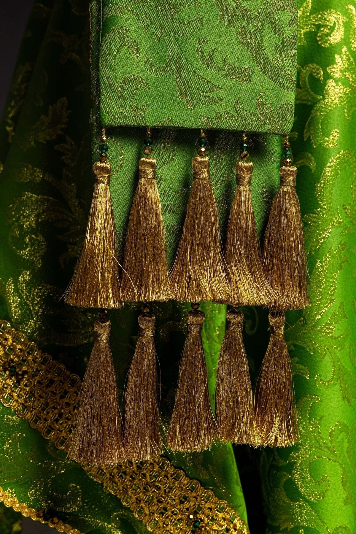 Green chasuble close-up showing gold tassel trim and bead details