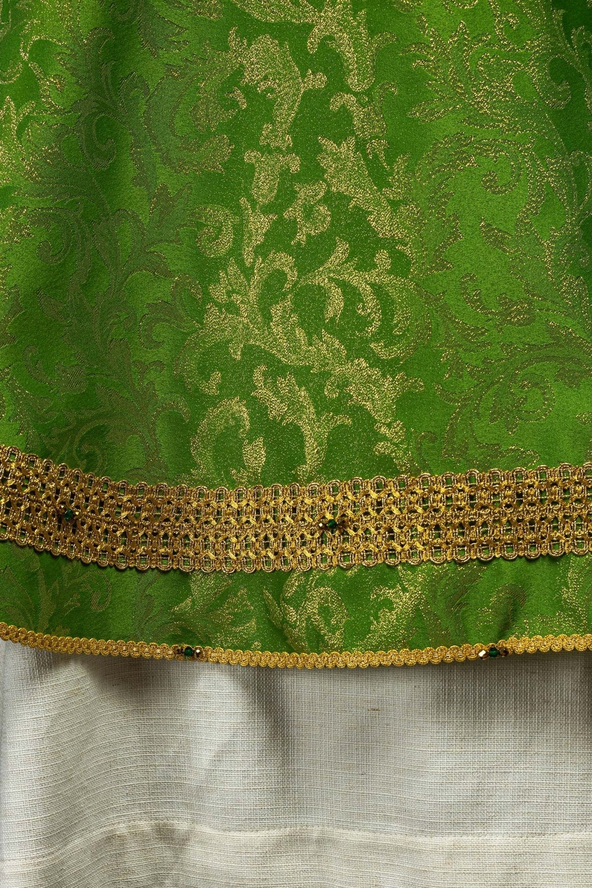 Green chasuble hem close-up with gold trim, green stones and white lining