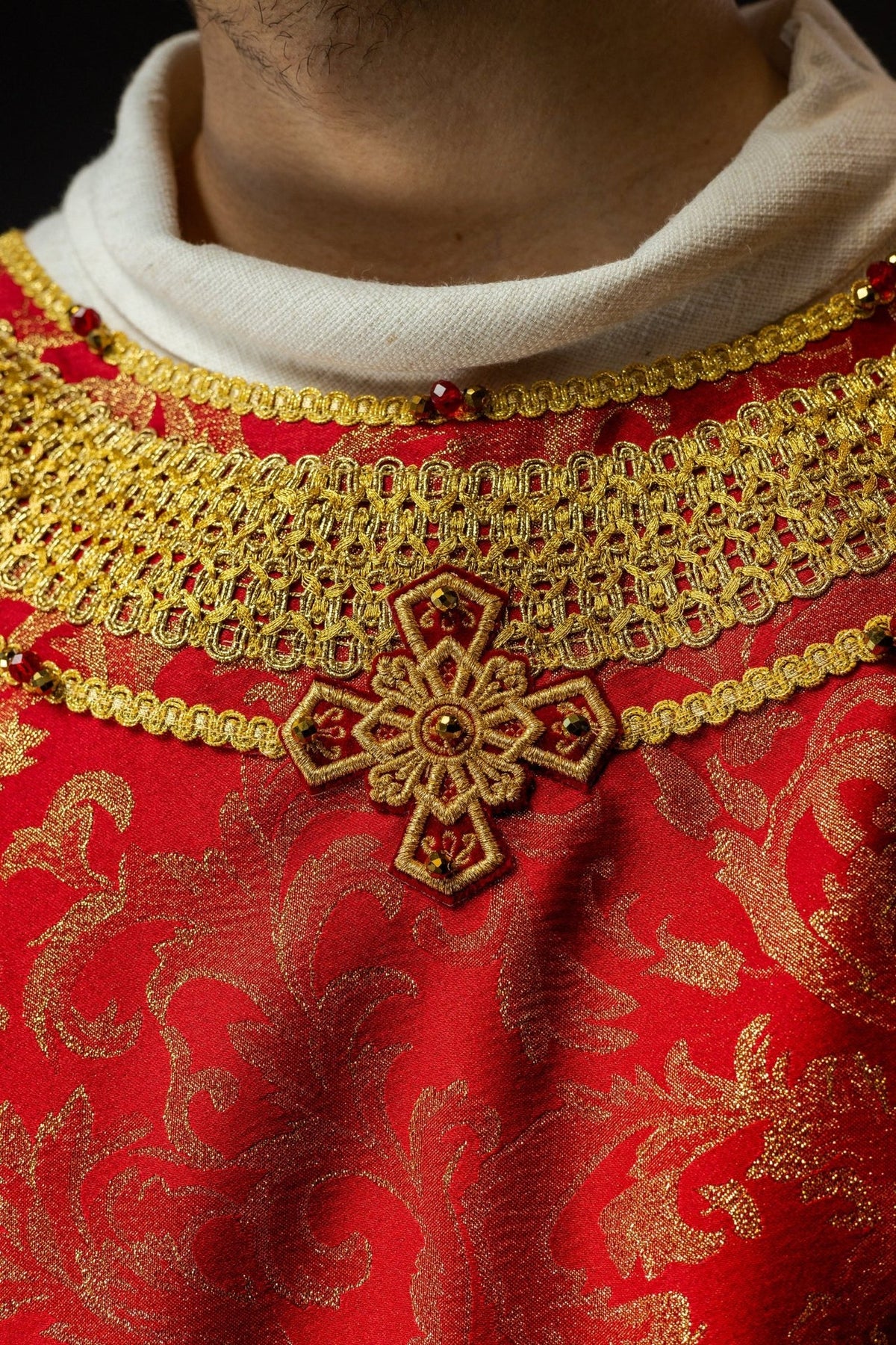Red chasuble close-up showing gold collar embroidery, cross and natural stones