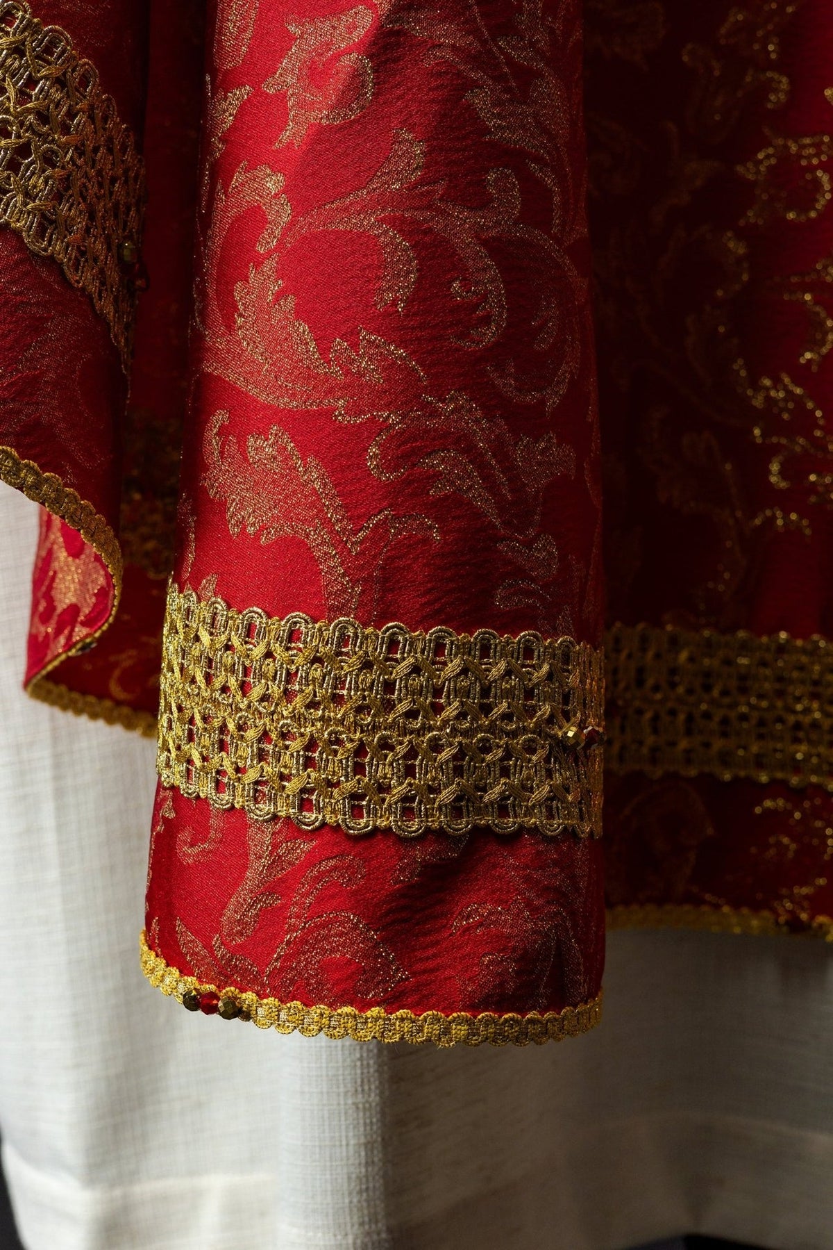 Red chasuble sleeve close-up with gold embroidery, red stones and trim