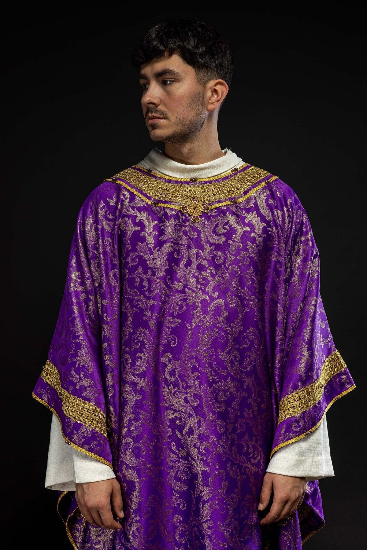 Purple chasuble worn front view with gold trim, cross embroidery and floral jacquard fabric