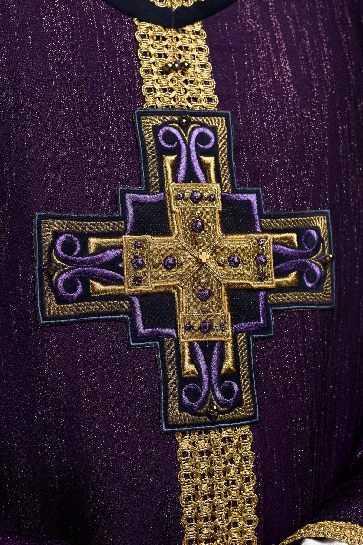 Purple chasuble close-up showing gold cross embroidery and natural stones