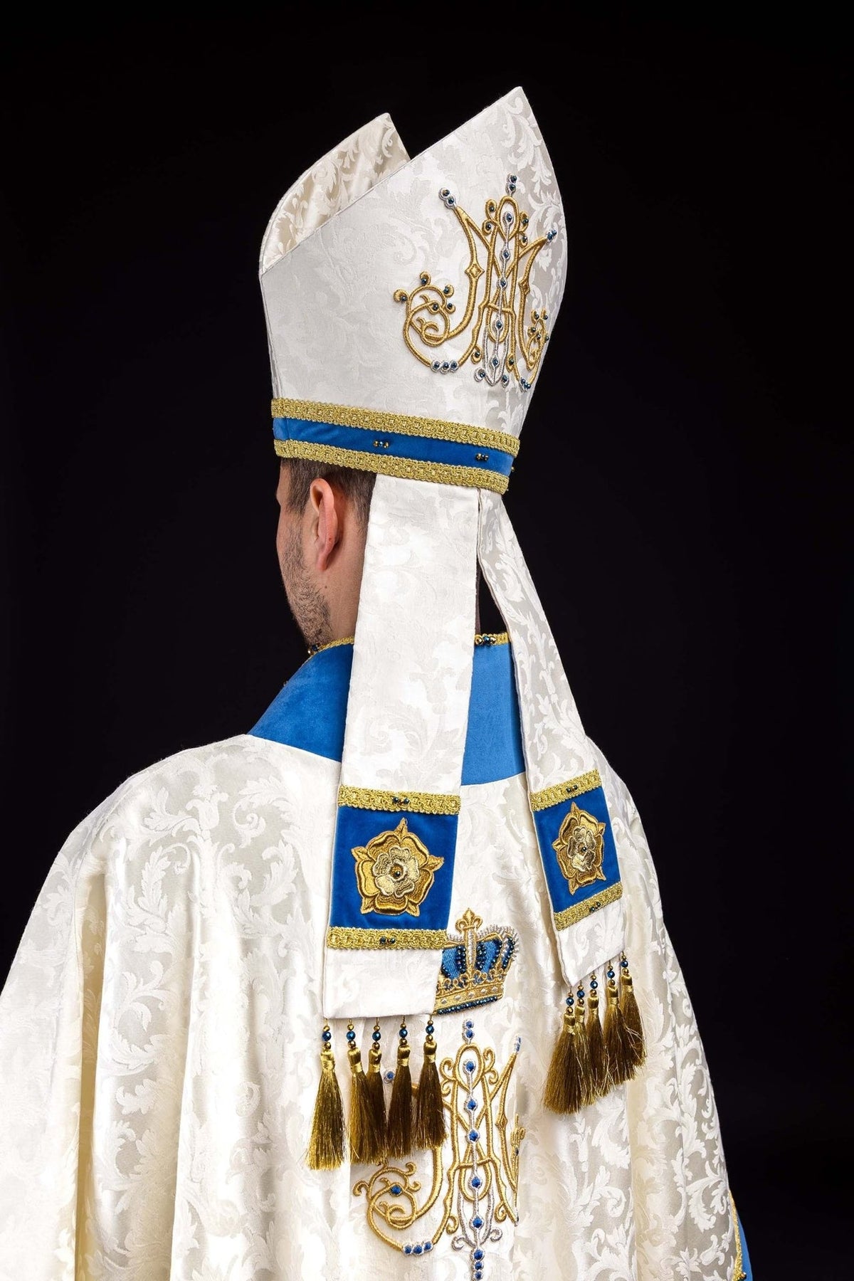 Marian miter in side view with ecru jacquard fabric, gold embroidery and blue band