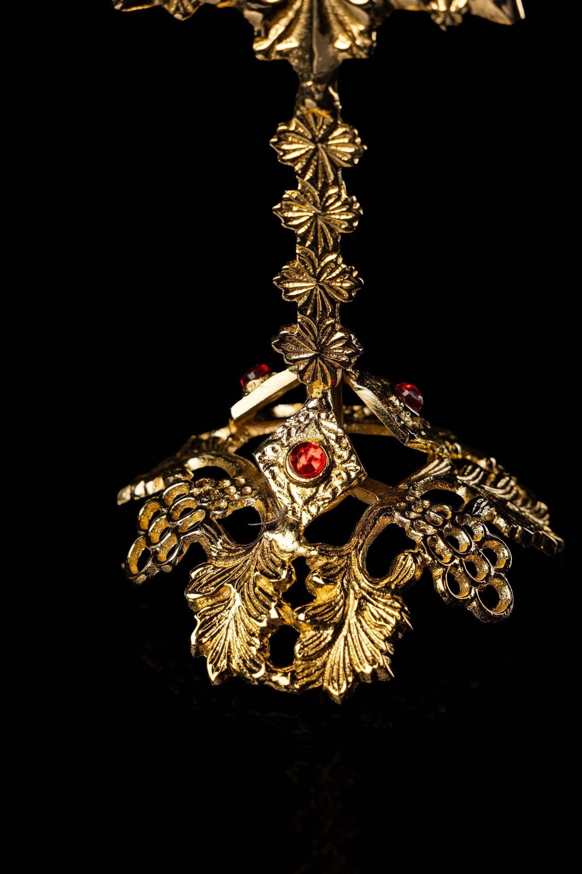 Brass reliquary close-up of floral stem, jeweled base, and red accents