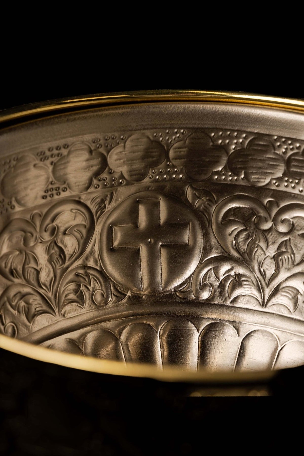 Brass holy water bucket detail with a raised cross and engraved floral decoration