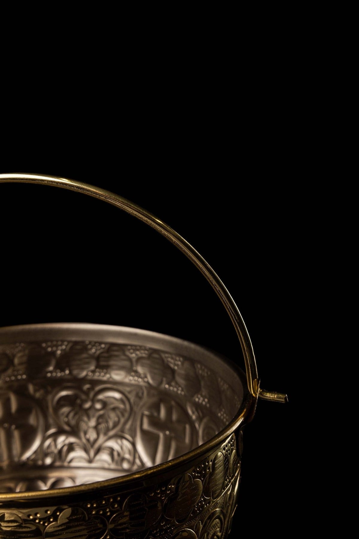 Brass holy water bucket close-up showing its curved handle and engraved interior
