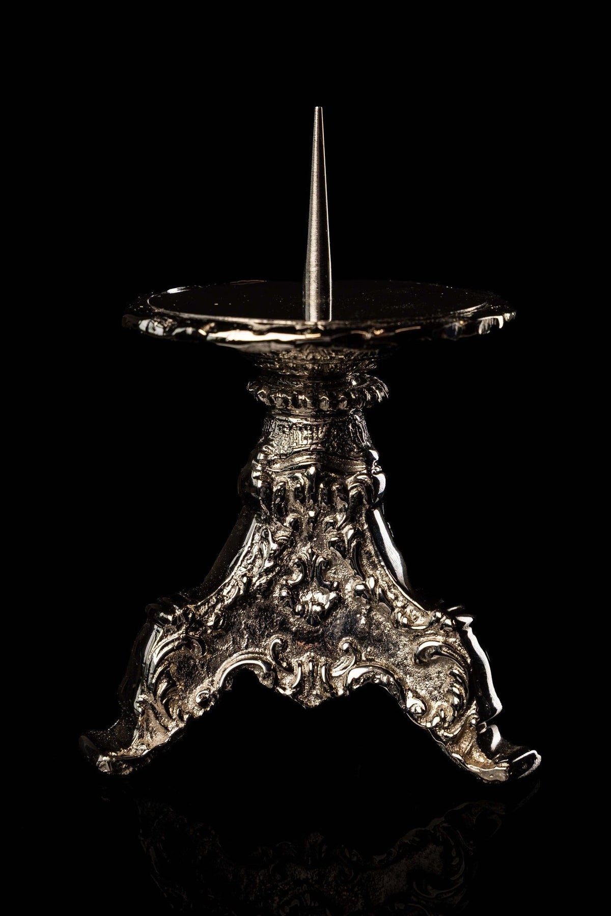 Nickel-plated brass candlestick front view with three curved feet and floral scrollwork