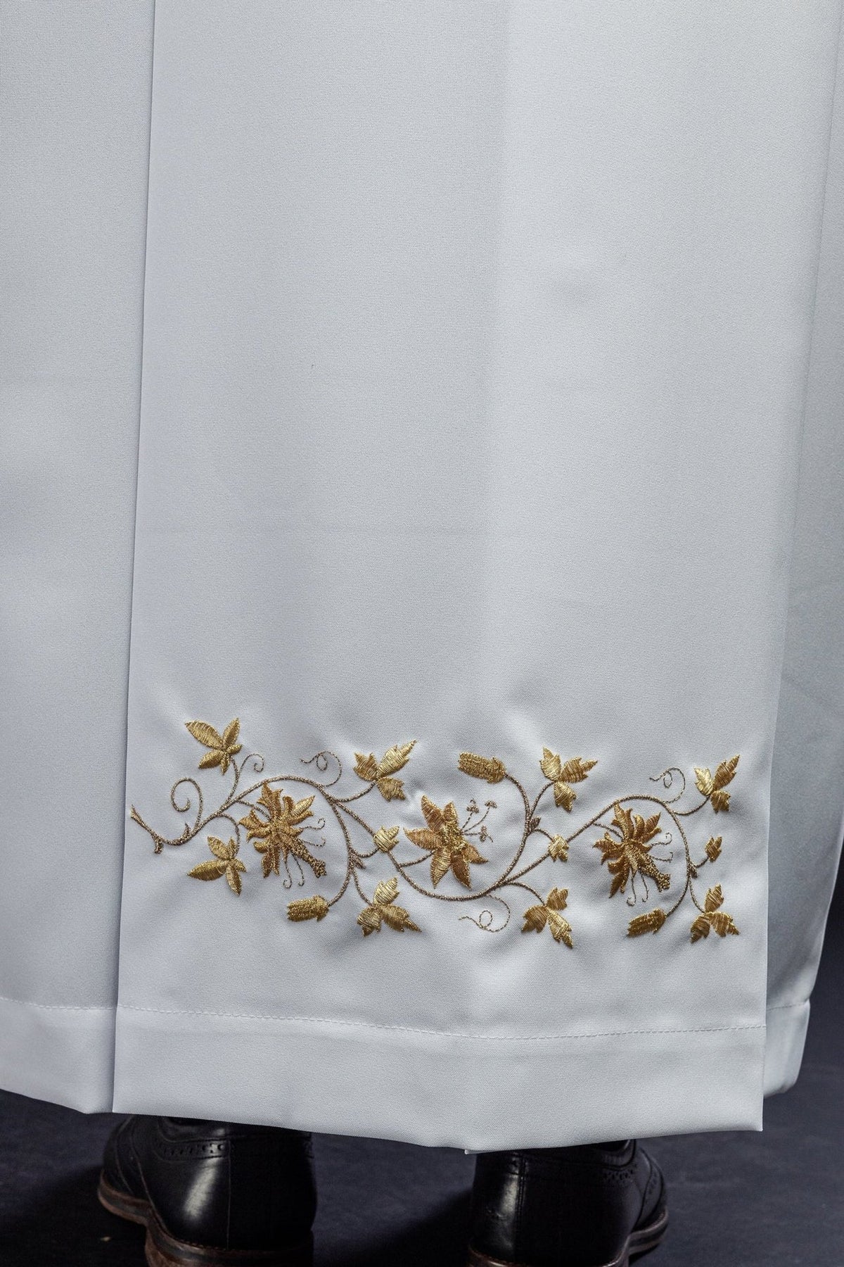 White priest alb close-up showing gold floral embroidery along the lower hem