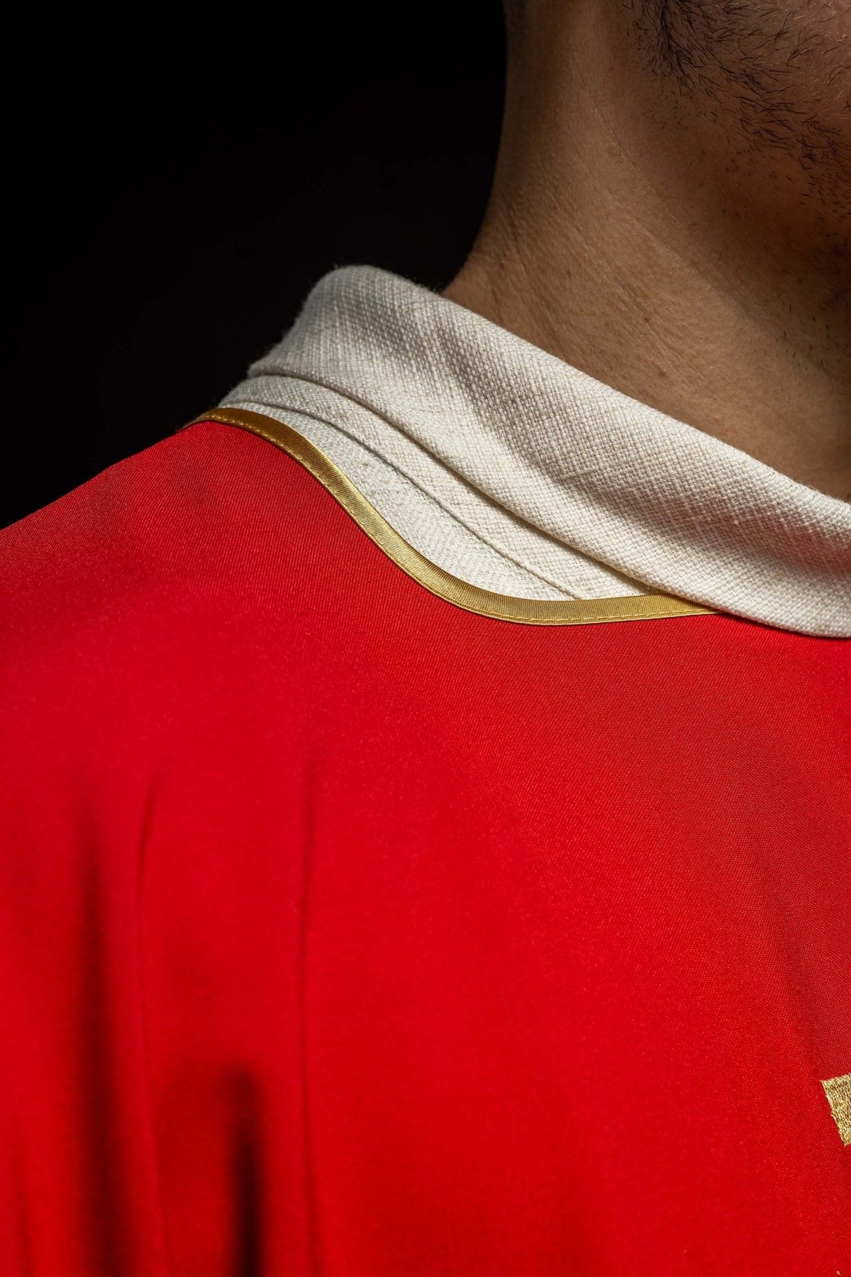 Red dalmatic close-up showing gold trim around the neckline and sleeve edge