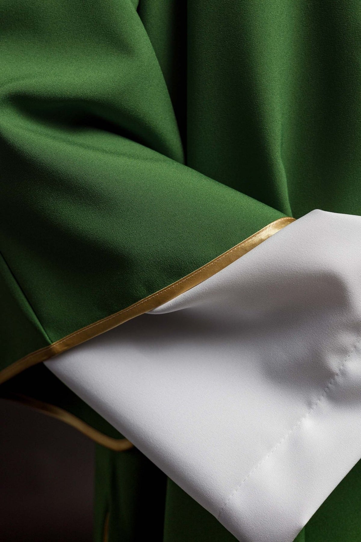 Green dalmatic close-up showing polyester fabric, gold trim and white cuff
