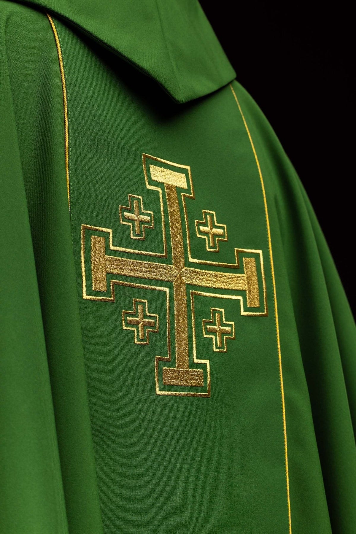 Green chasuble close-up showing gold trim, embroidered cross and wide sleeves