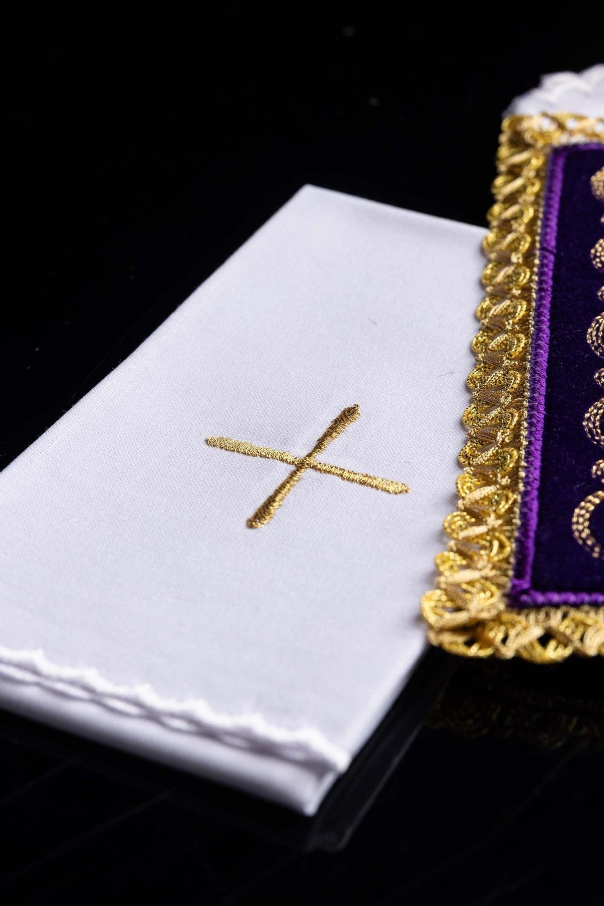 White altar linen close-up with gold cross embroidery beside the purple velvet pall