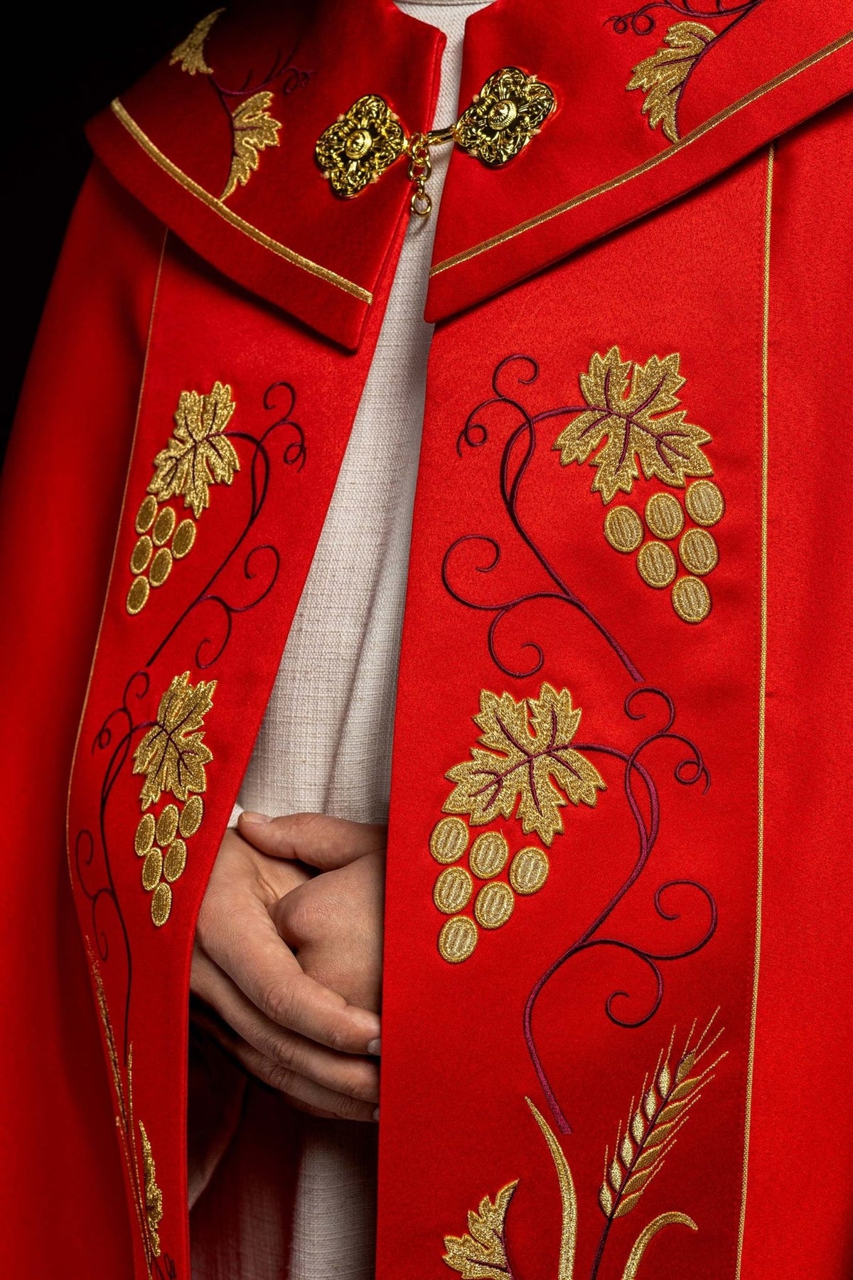 Red cope close-up showing gold floral clasp and grapes embroidery