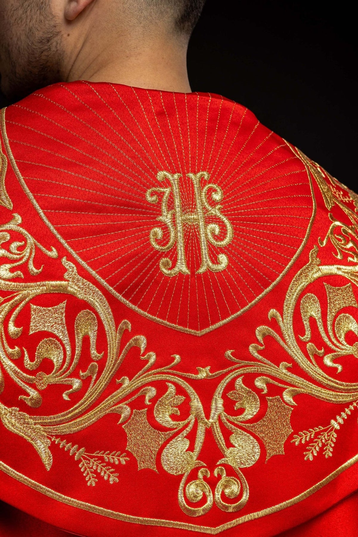 Red cope, close-up back view of gold IHS embroidery and radiating lines