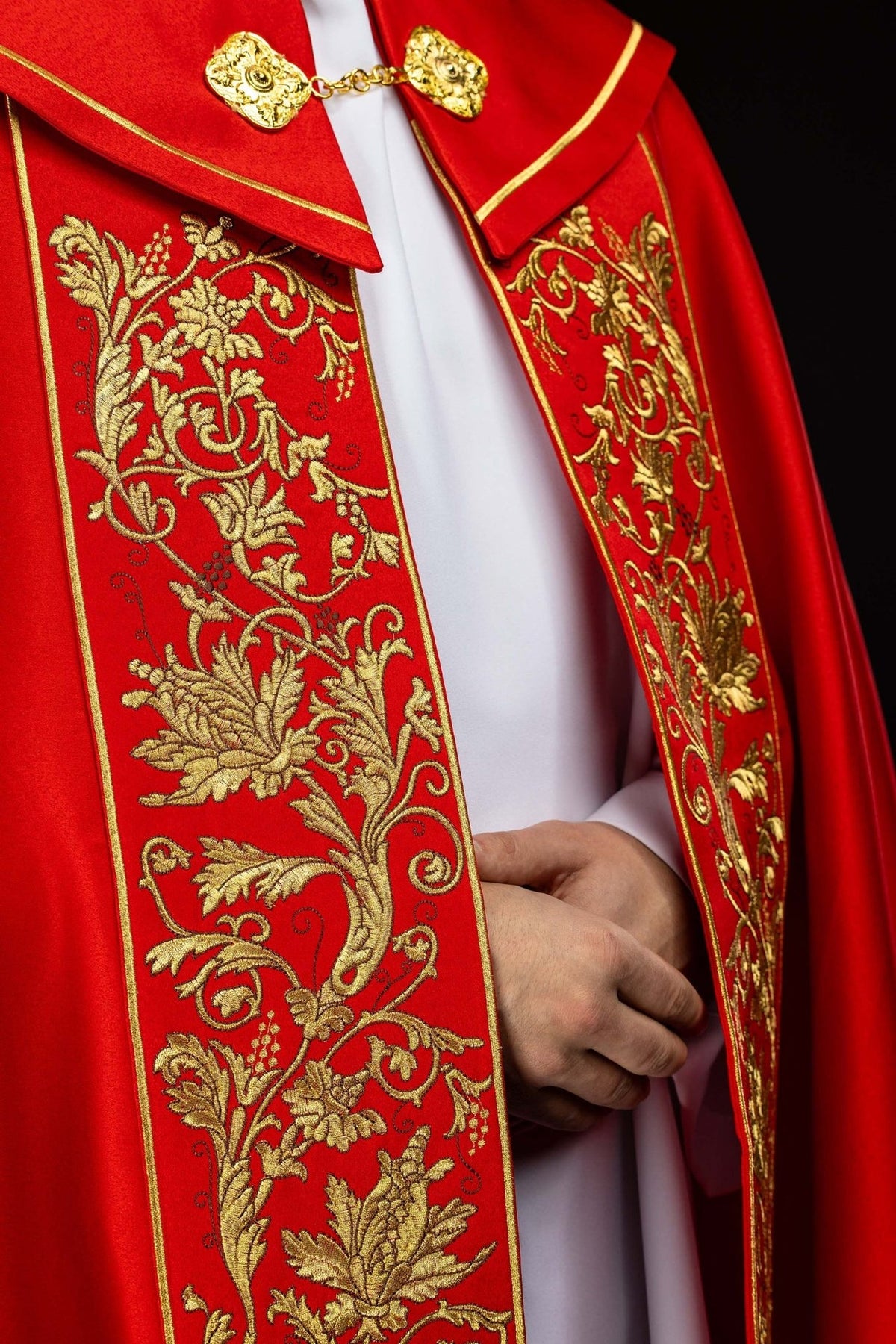 Red liturgical cope close-up showing gold floral embroidery and ornate fastening