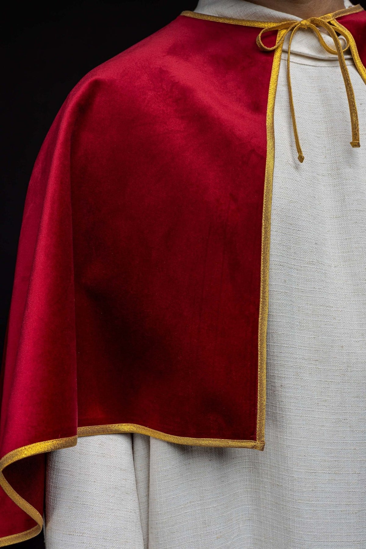 Red velvet cape close-up showing the gold trim along the edge and front opening