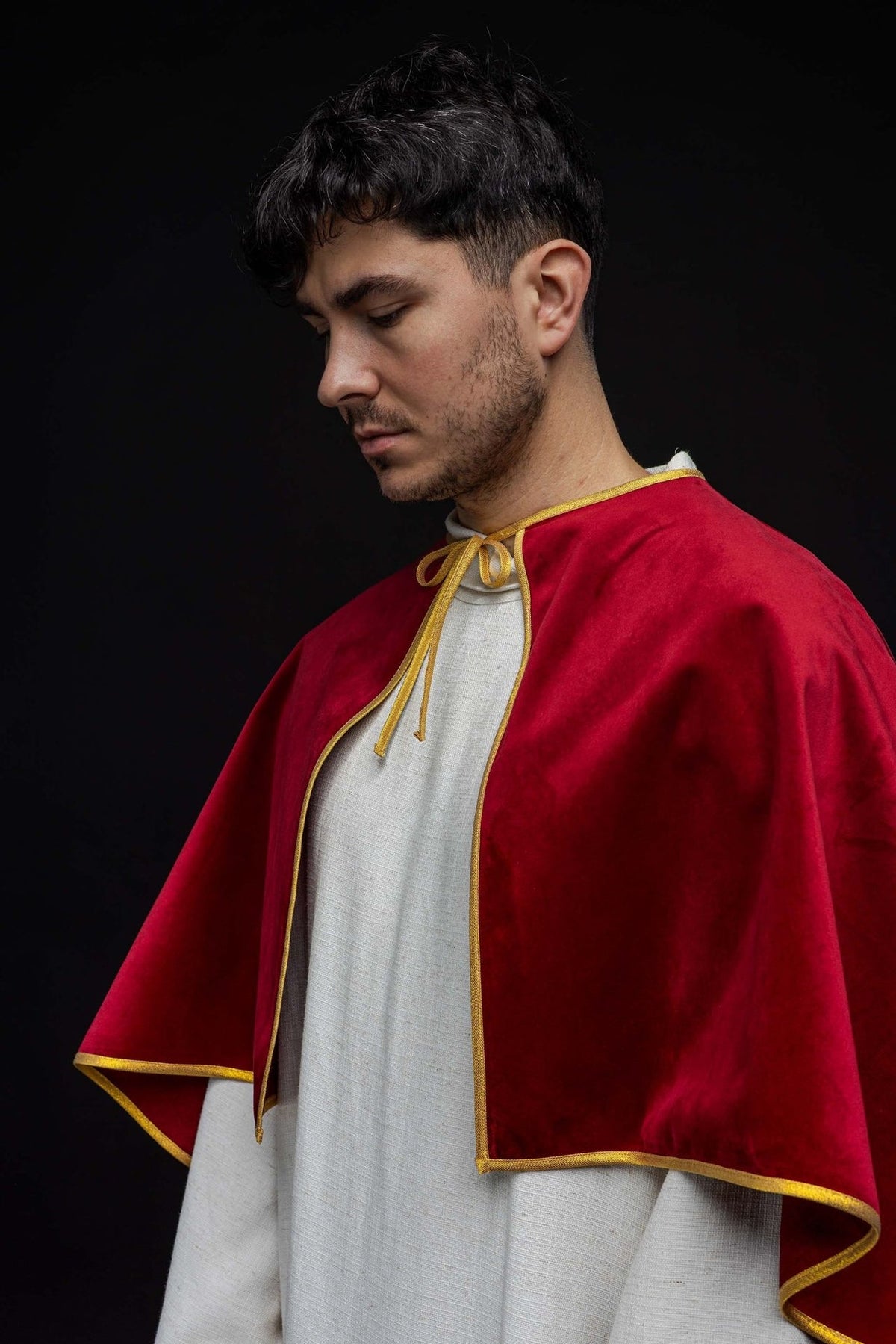 Red velvet cape worn from the side, showing the flowing shape and gold-edged opening