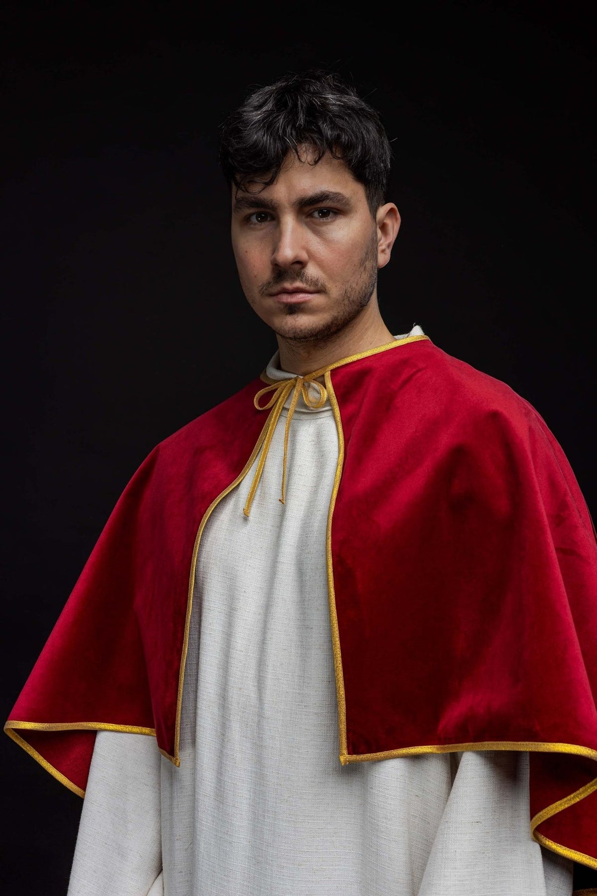Red velvet cape worn from the front at an angle, showing the gold-edged hem