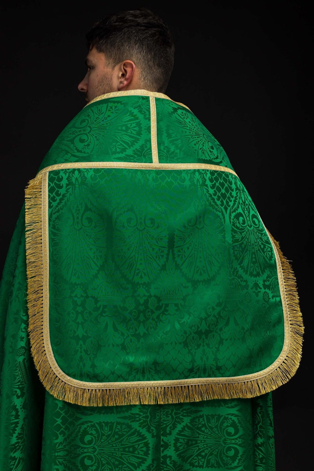 Green jacquard cope shown from the back with gold trim, fringe and ornate woven motifs