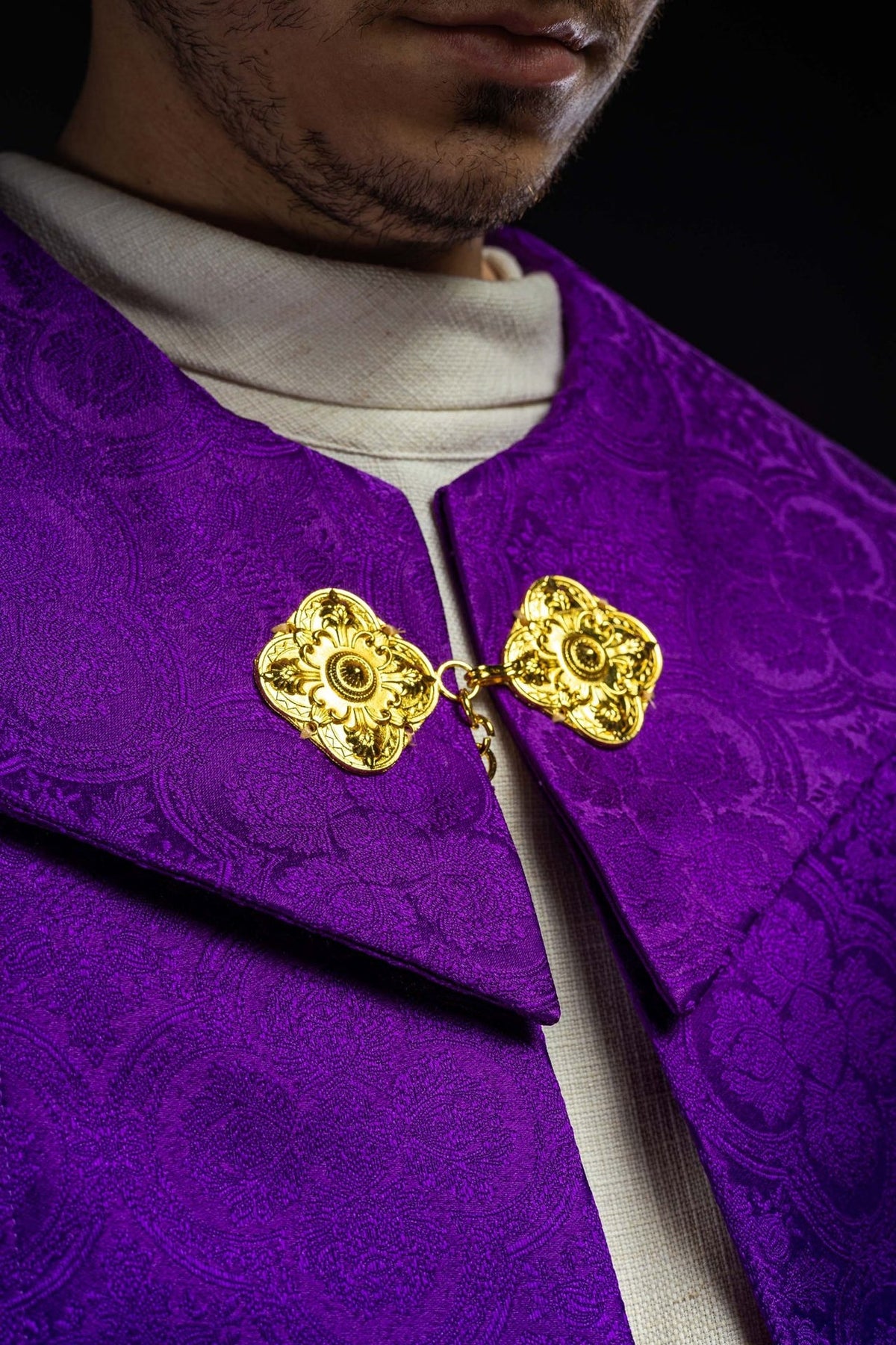 Purple cope close-up showing ornate gold front clasps and woven jacquard fabric