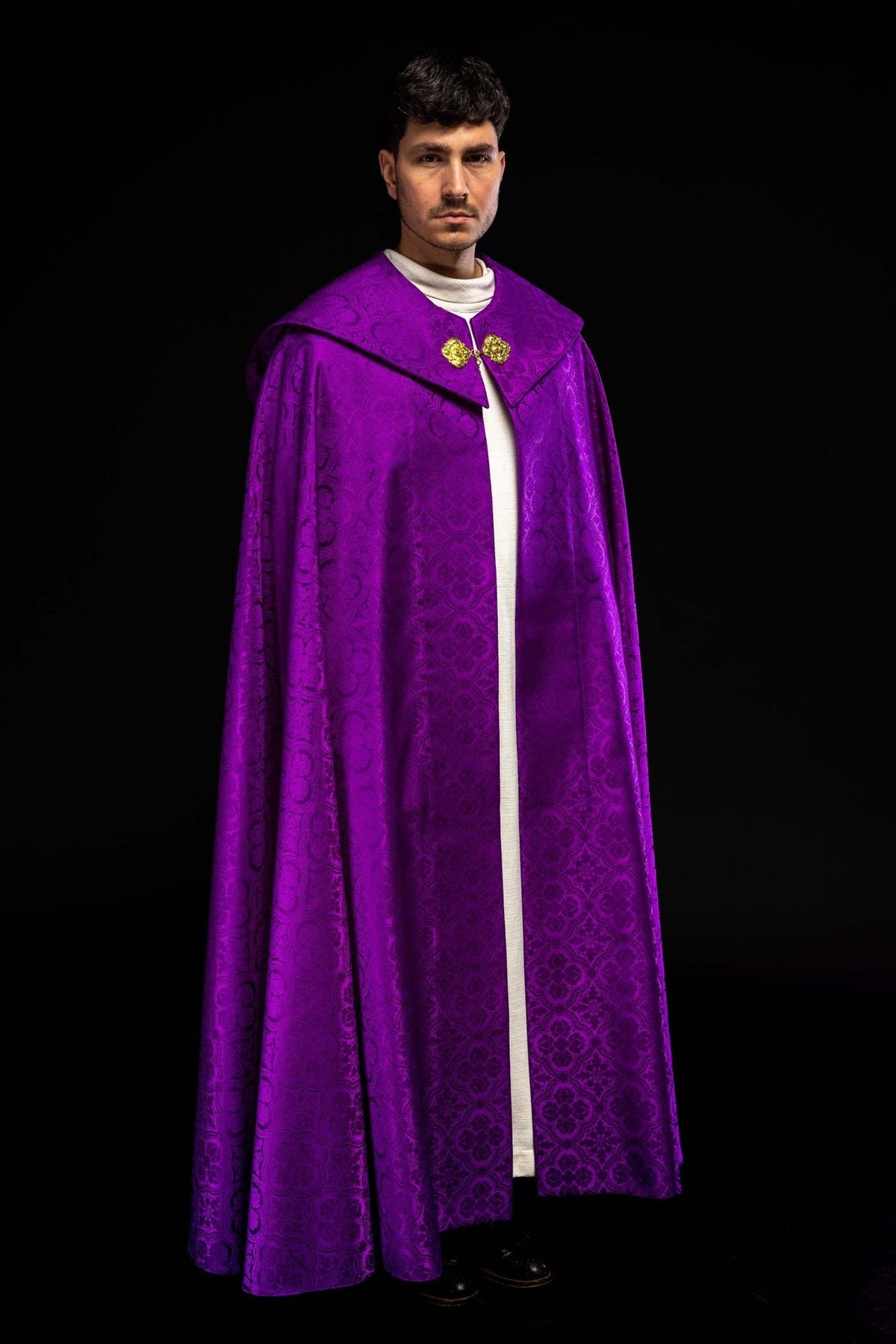 Purple cope worn from a three-quarter front view with gold clasps and patterned fabric