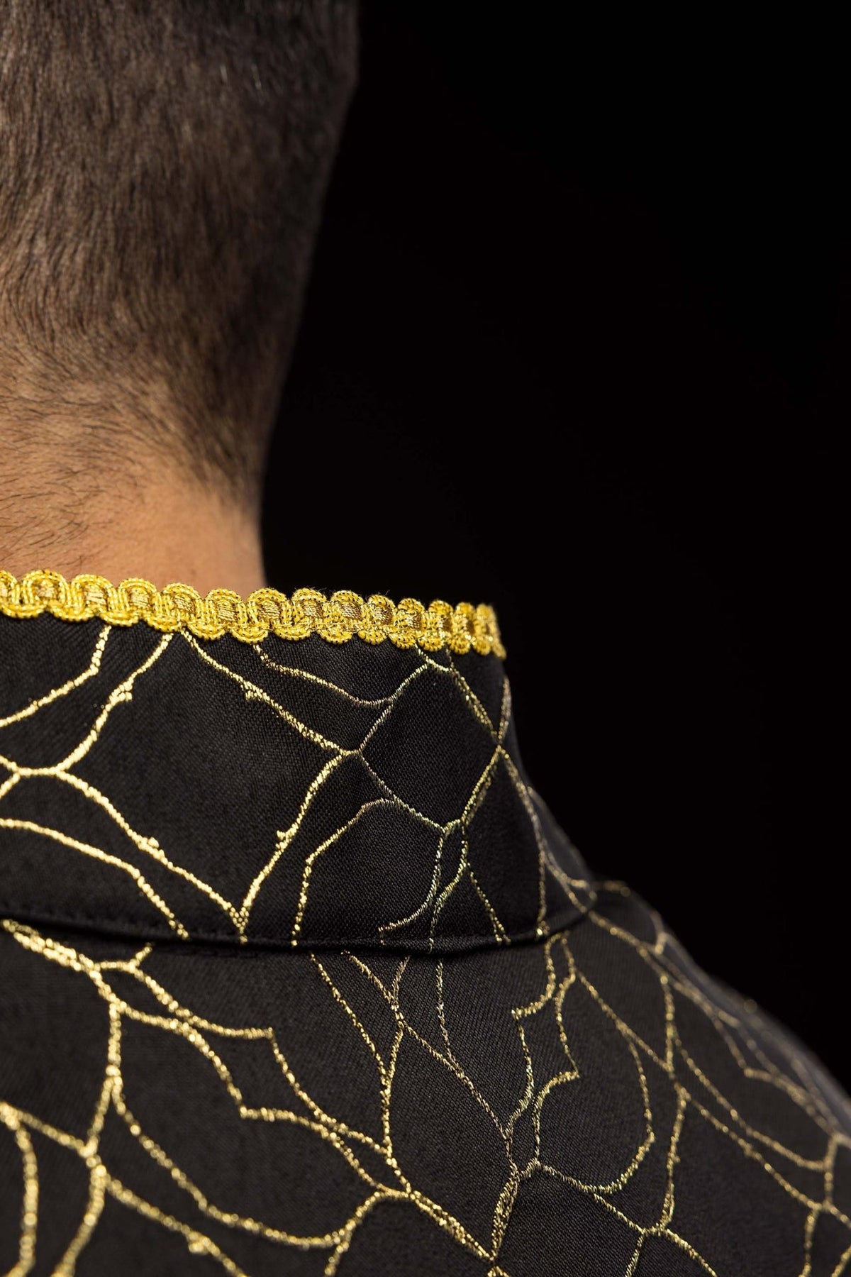 Black cope collar close-up with gold trim and floral jacquard fabric