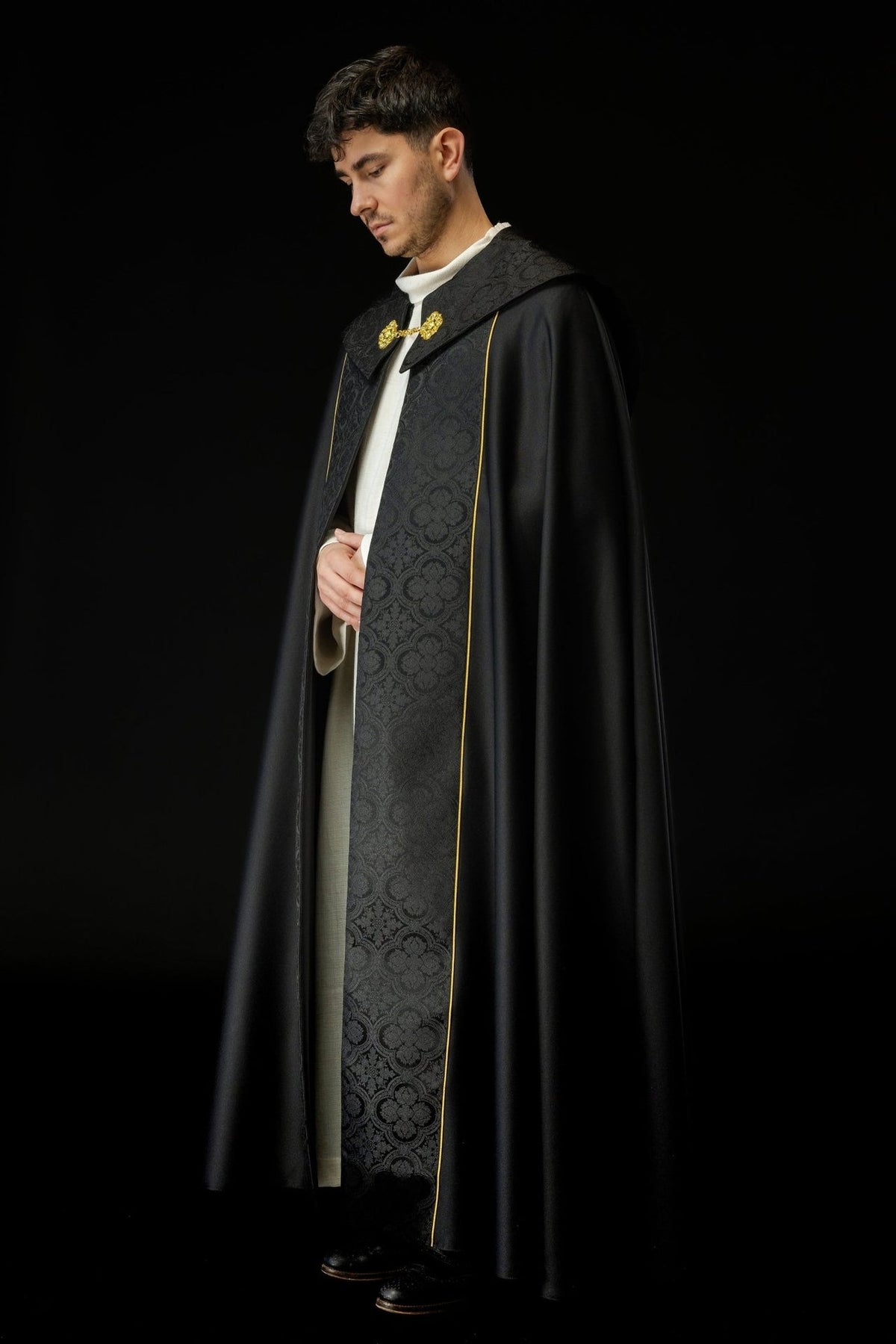 Black cope worn from the side, showing flowing satin fabric and jacquard front panel
