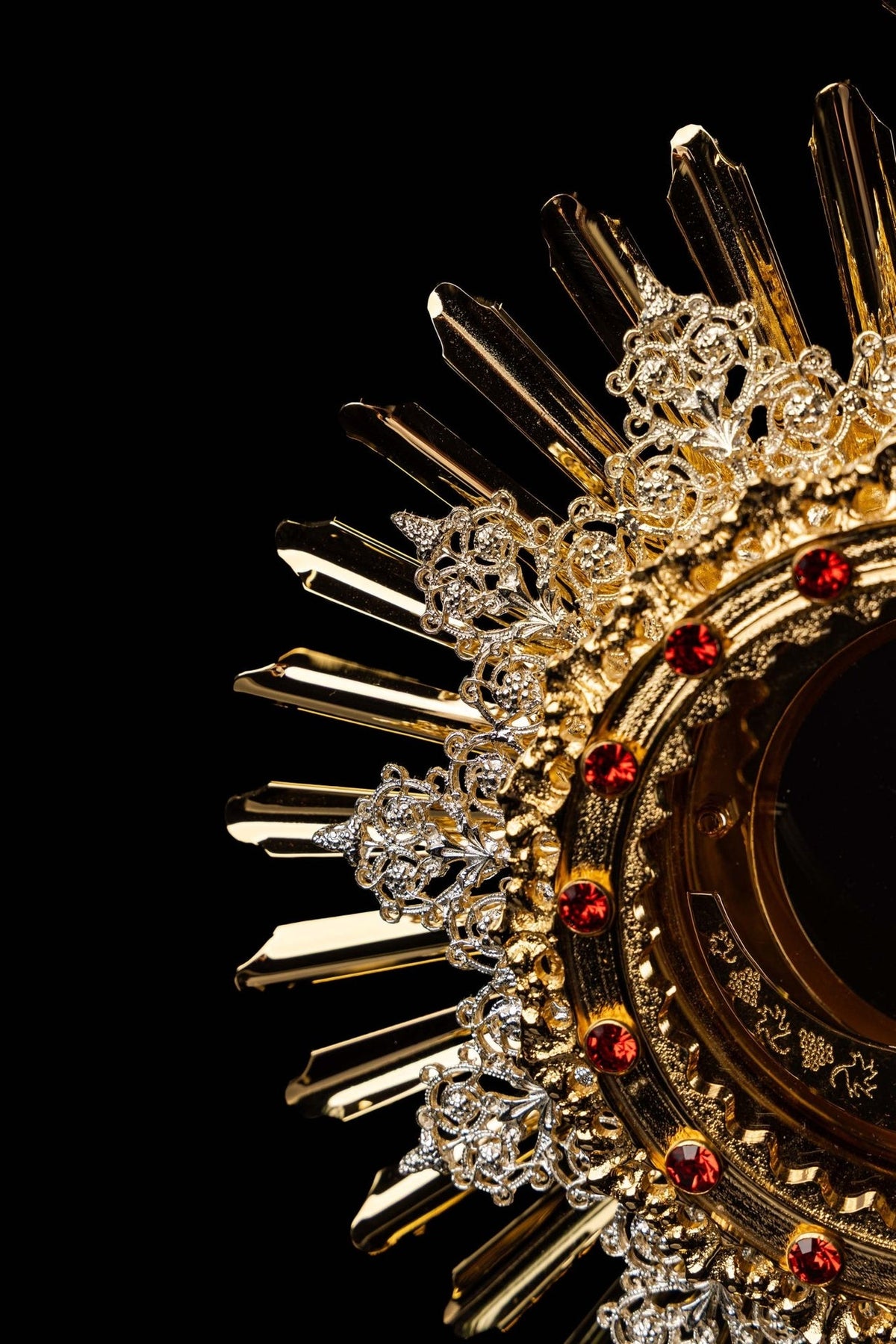 Monstrance angled close-up showing engraved IHS emblem and ruby-studded rim