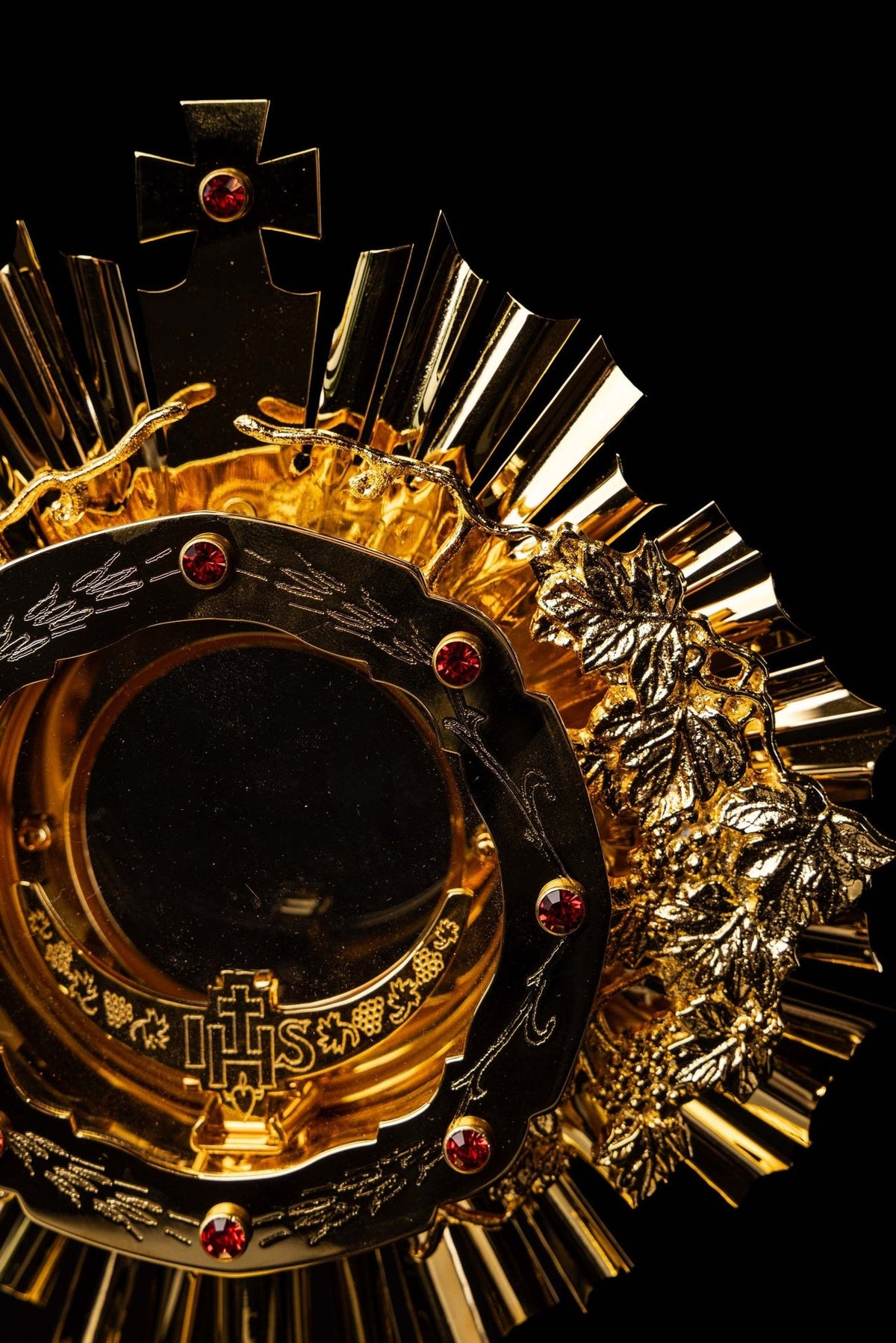 Catholic monstrance angled close-up showing cross, rays, grapevine and red gemstones