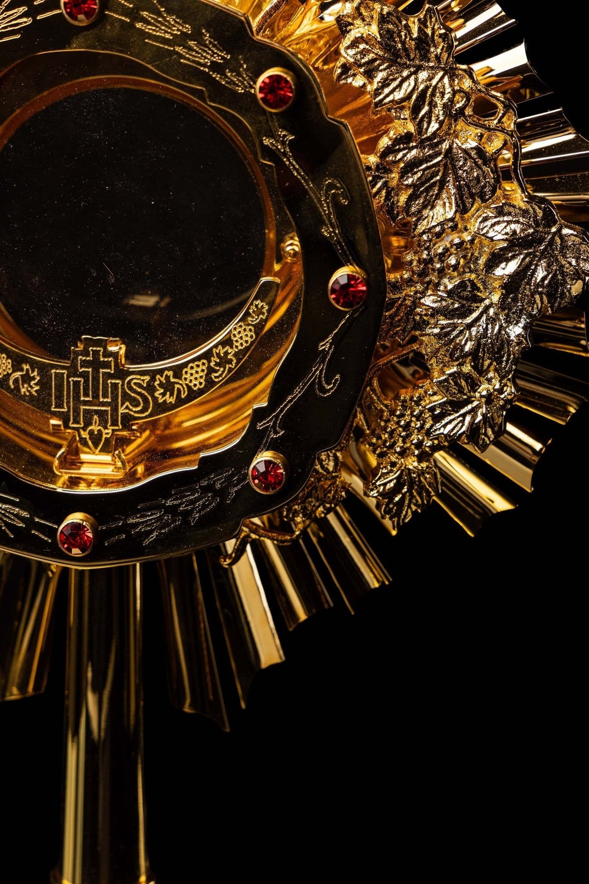 Catholic monstrance close-up showing grapevine relief, IHS symbol and red gemstones