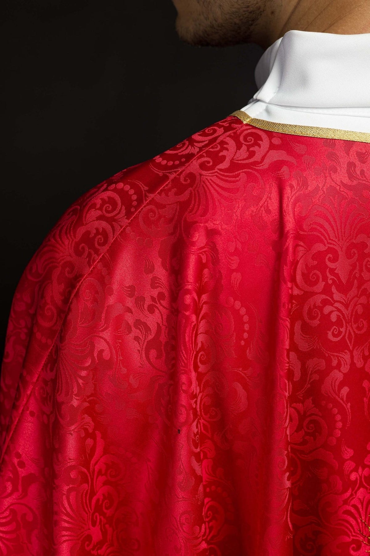 Red jacquard chasuble close-up with ornate woven pattern and gold trim
