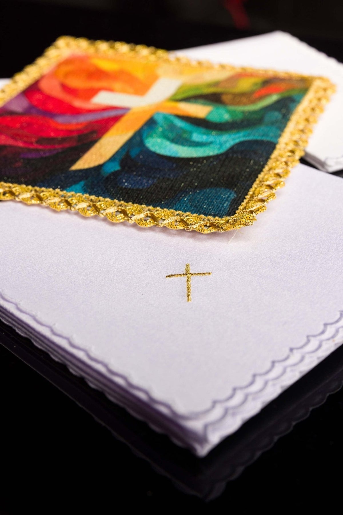 Altar linen set showing colorful cross panel over folded white linen with gold cross