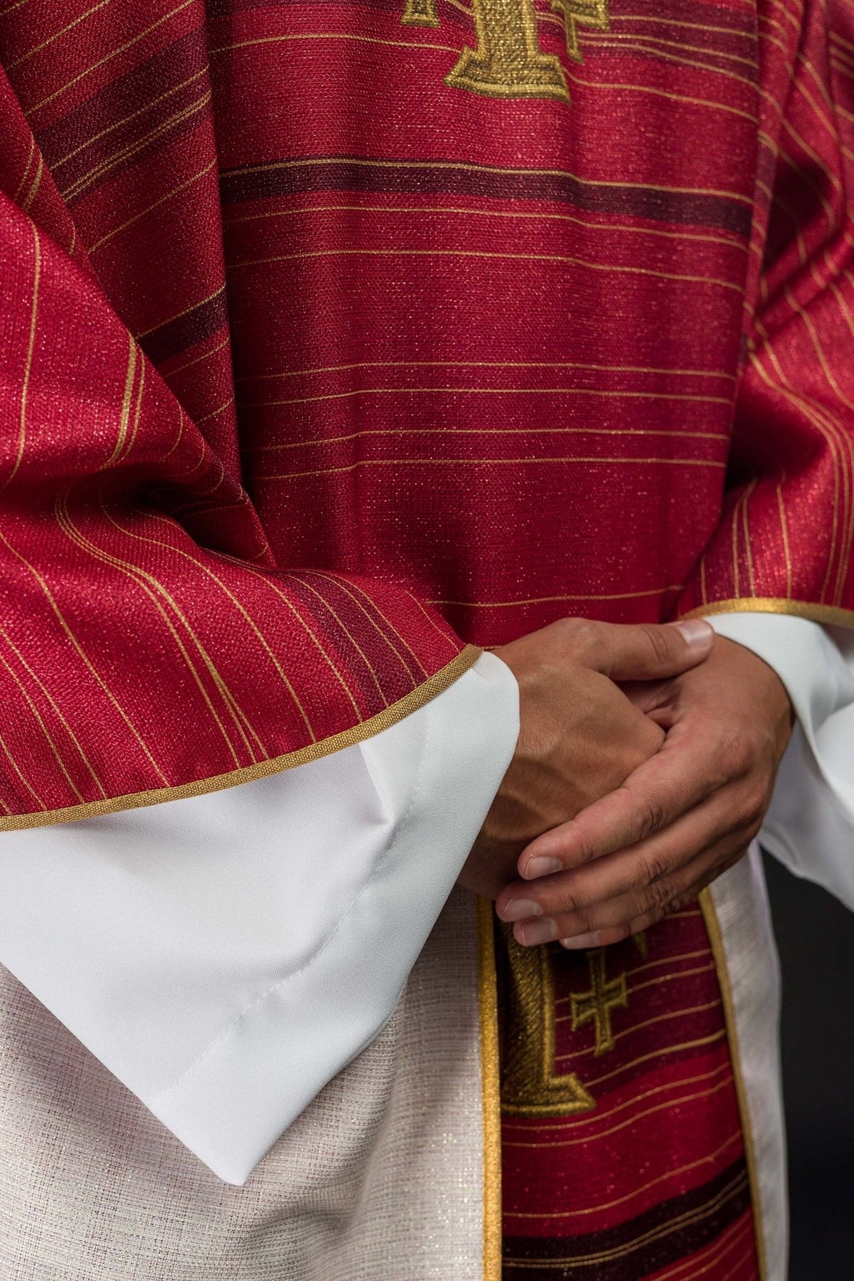 Red chasuble fabric close-up with horizontal gold stripes and dark accent bands