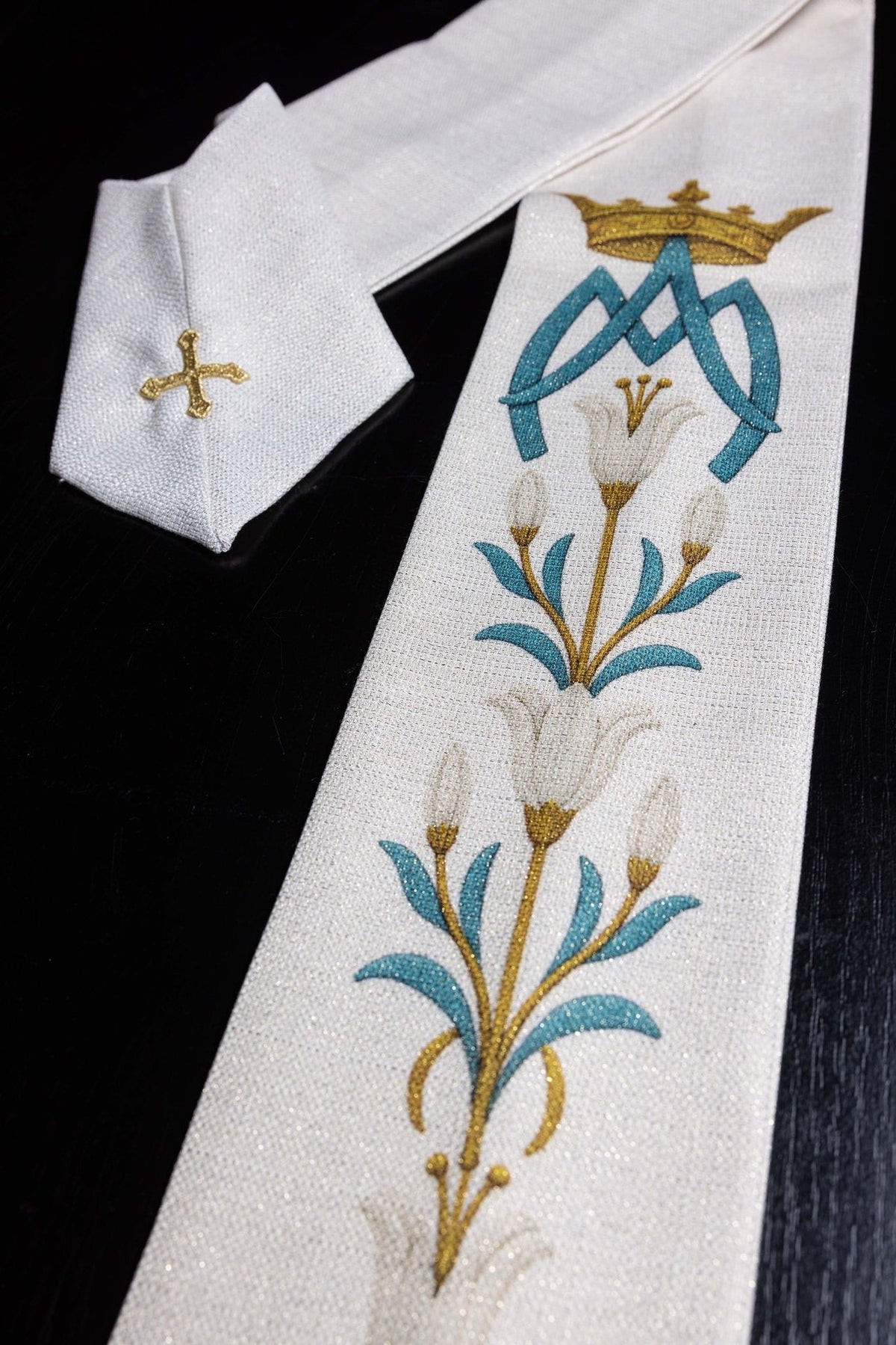 Marian chasuble close-up with white fabric, blue and gold lily pattern, and Our Lady monogram