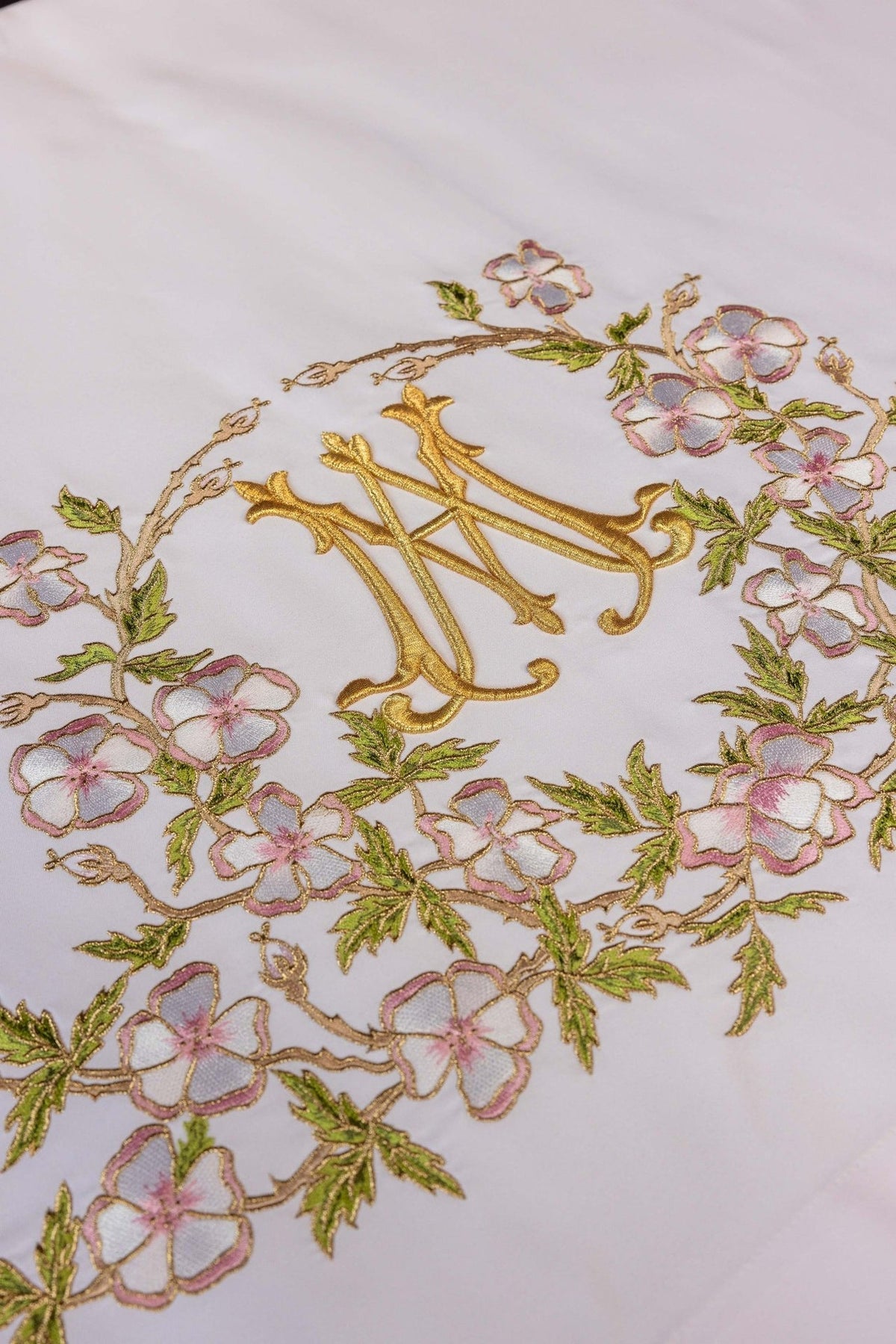 Altar cloth close-up showing gold Marian embroidery surrounded by pink flowers and green leaves