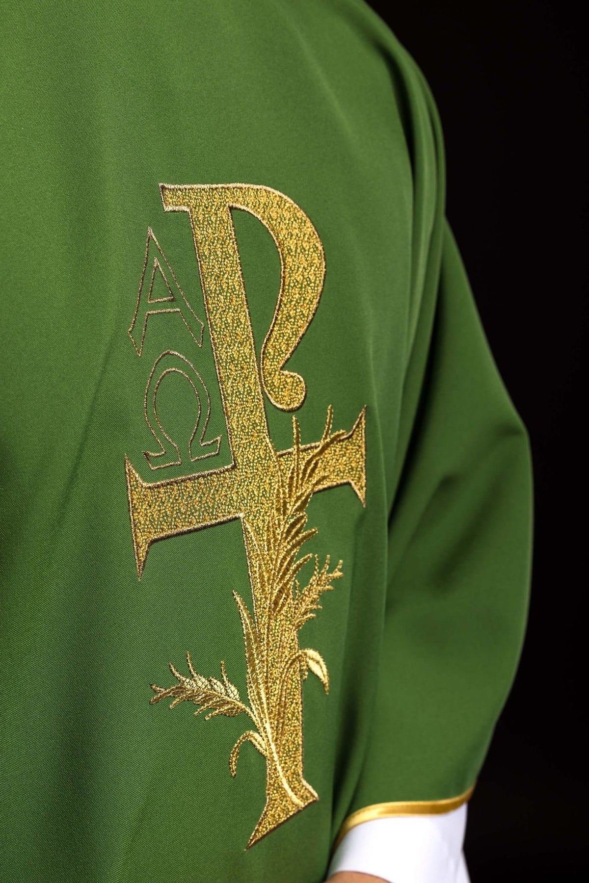 Green chasuble close-up showing gold Alpha Omega cross embroidery