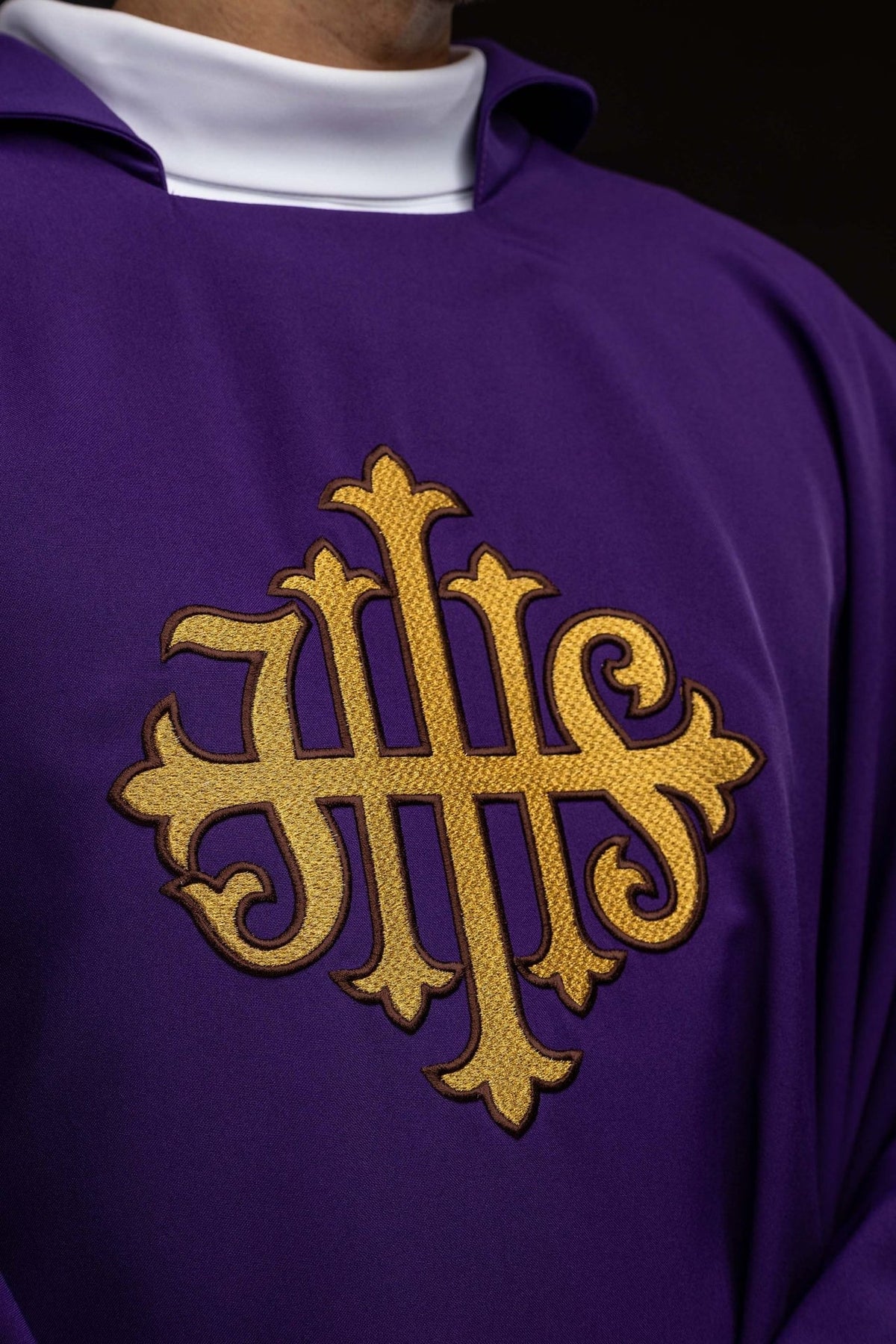 Purple chasuble close-up showing gold JHS embroidery on the front
