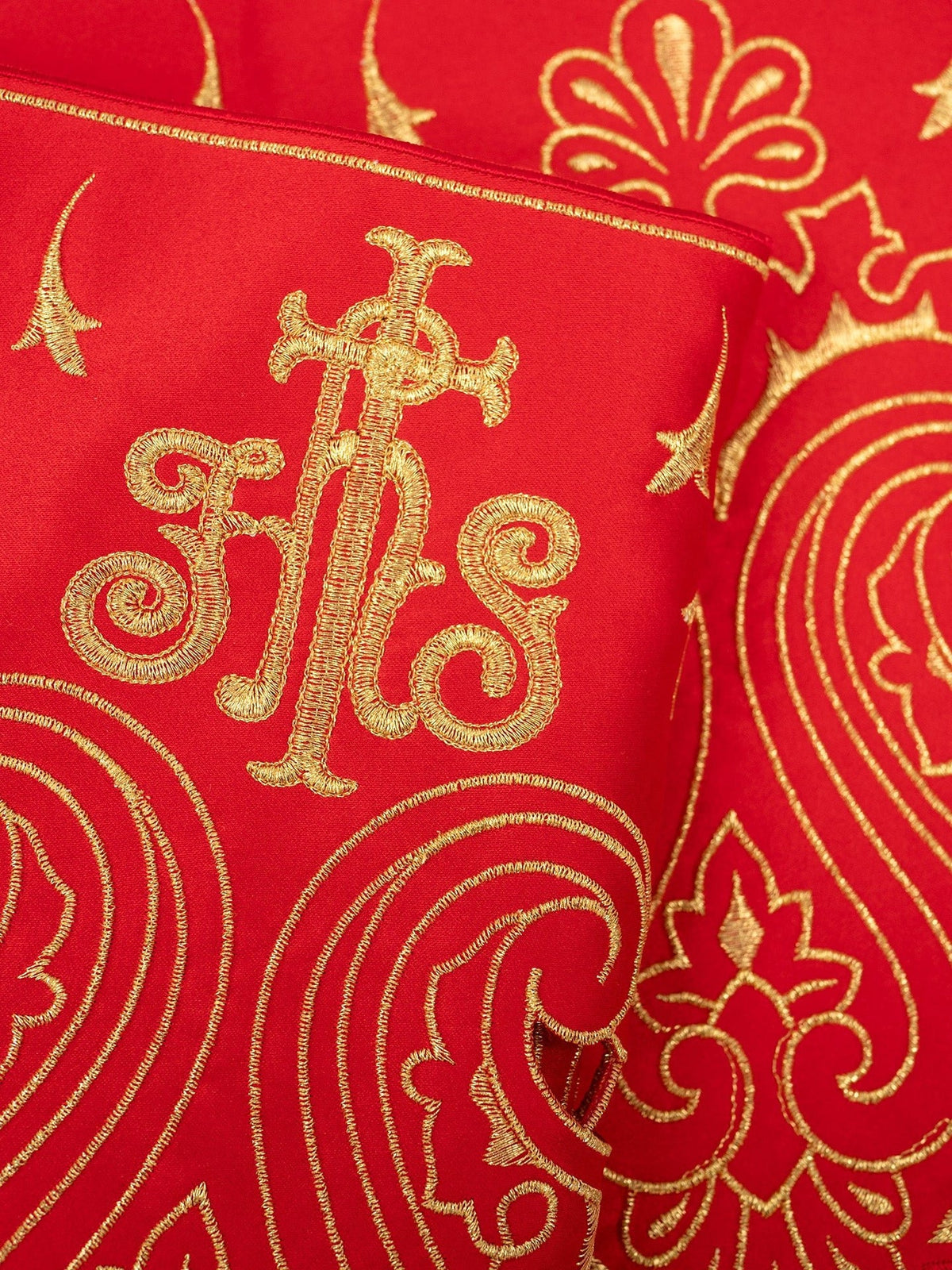 Red altar lace close-up showing gold IHS embroidery and ornate scrolling motifs