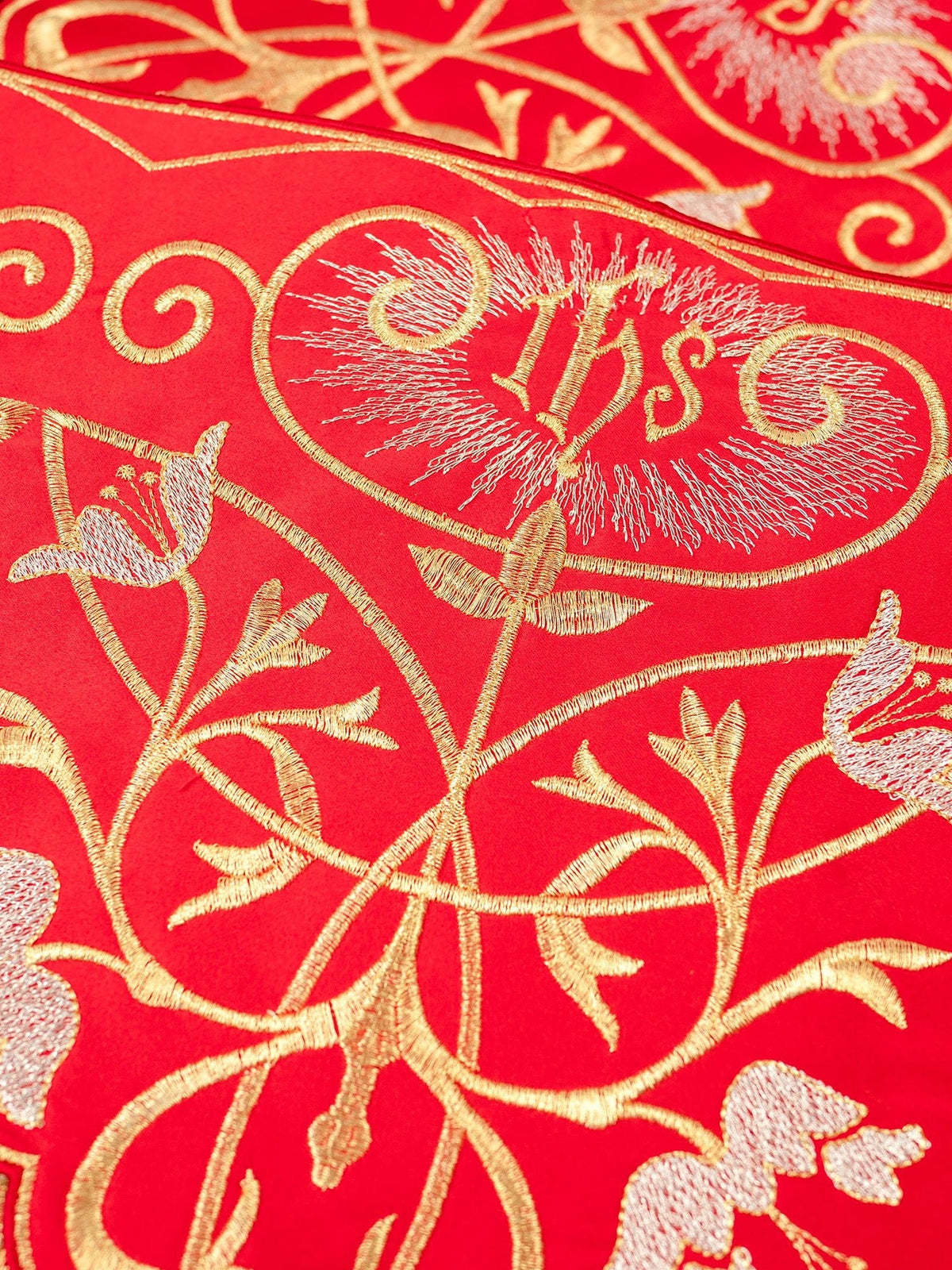 Red altar lace close-up showing embroidered IHS monogram, gold scrolls and floral details