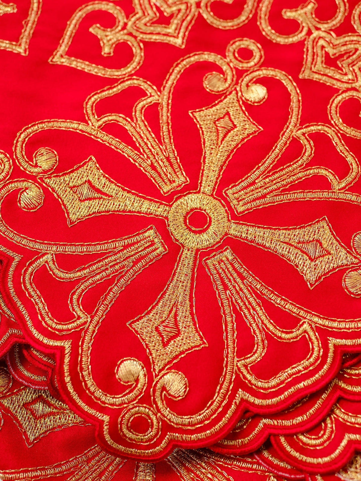 Red altar lace close-up showing gold rosette embroidery and scalloped edge
