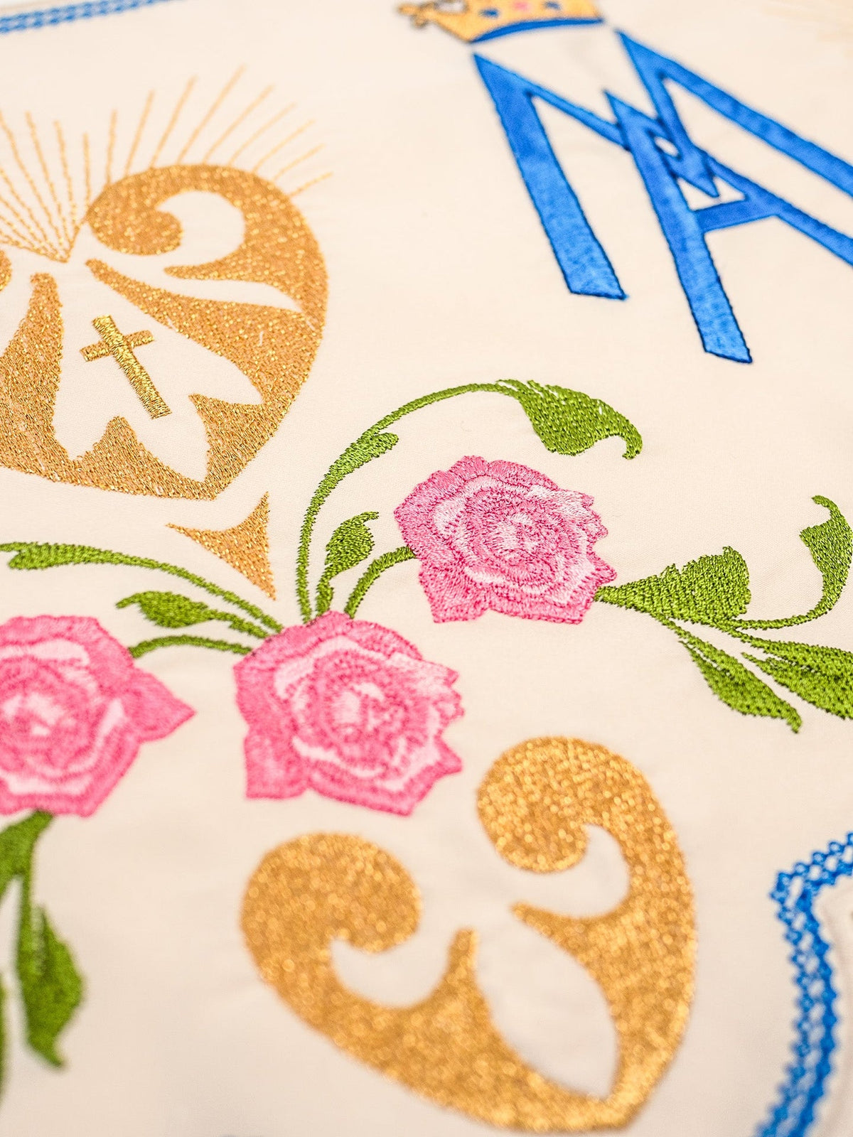 Altar lace close-up showing Marian motif embroidery with gold hearts, pink roses and blue edging