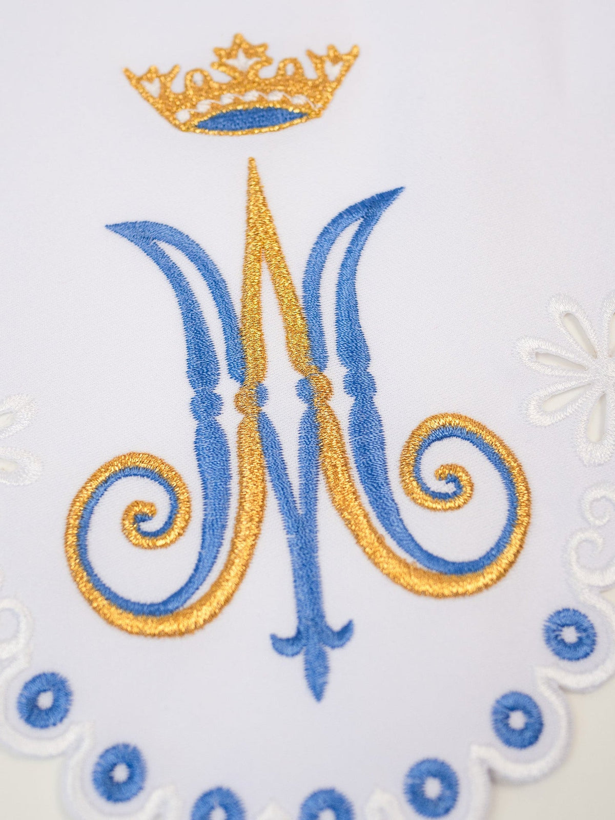 Altar lace close-up showing blue and gold Marian motif embroidery with crown and scalloped edging