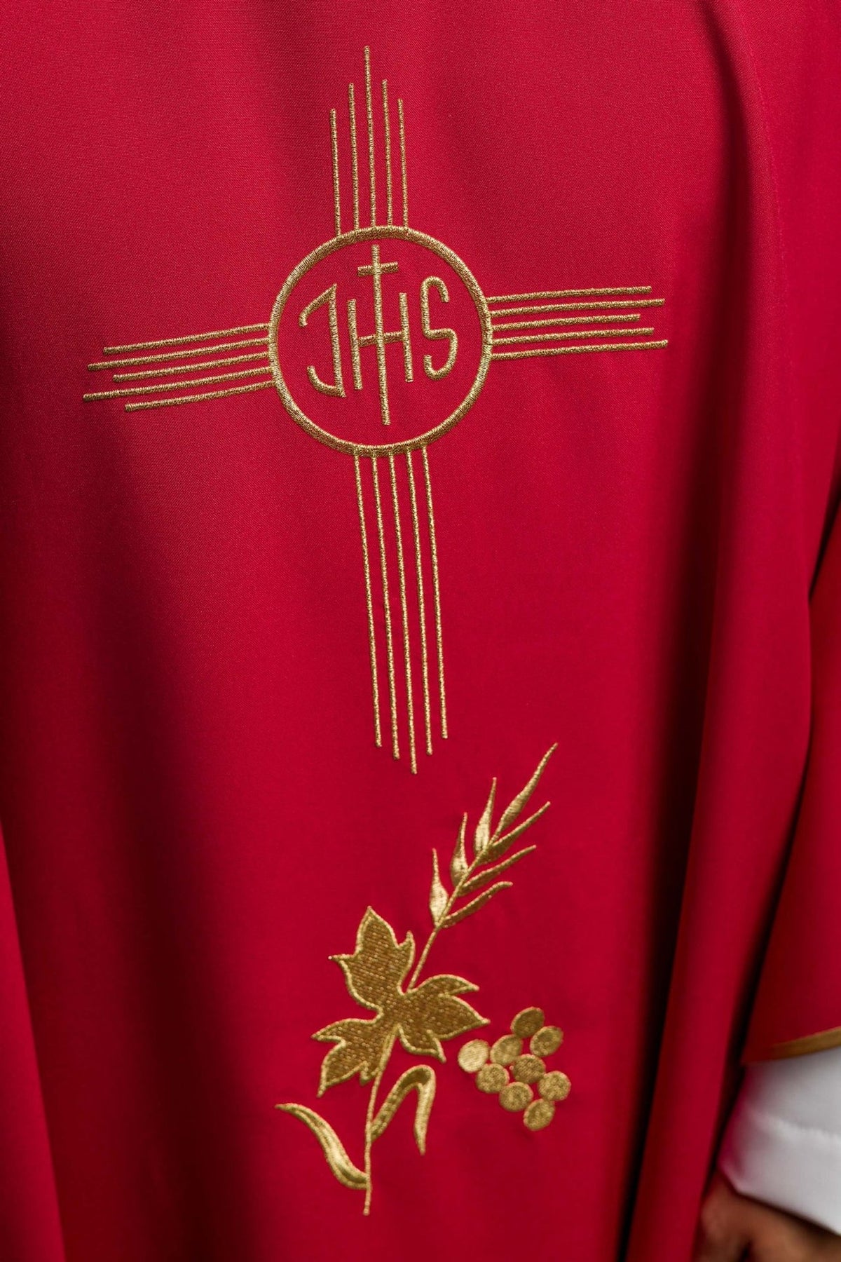 Red chasuble close-up showing gold embroidered IHS motif and floral embroidery