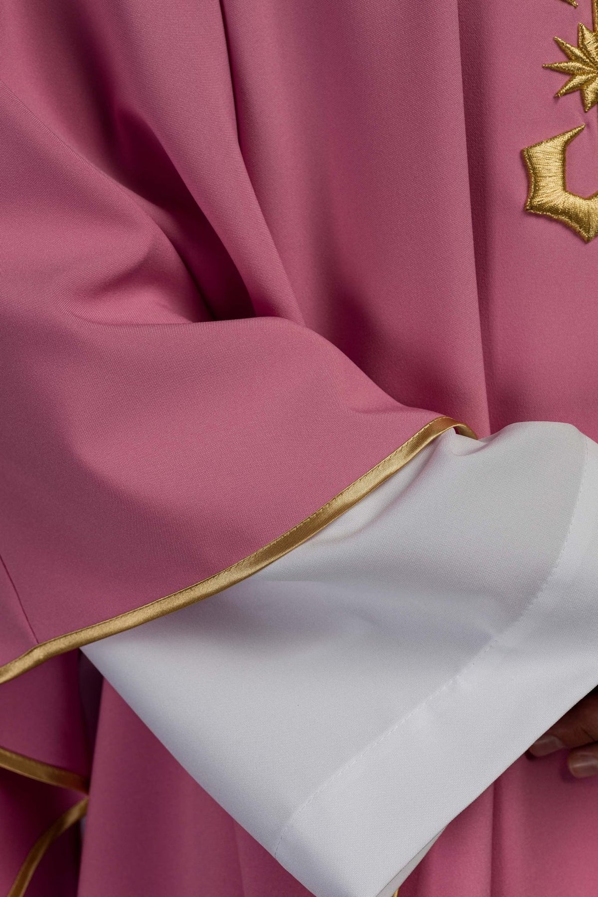 Rose chasuble detail showing fabric folds, gold trim and IHS embroidery