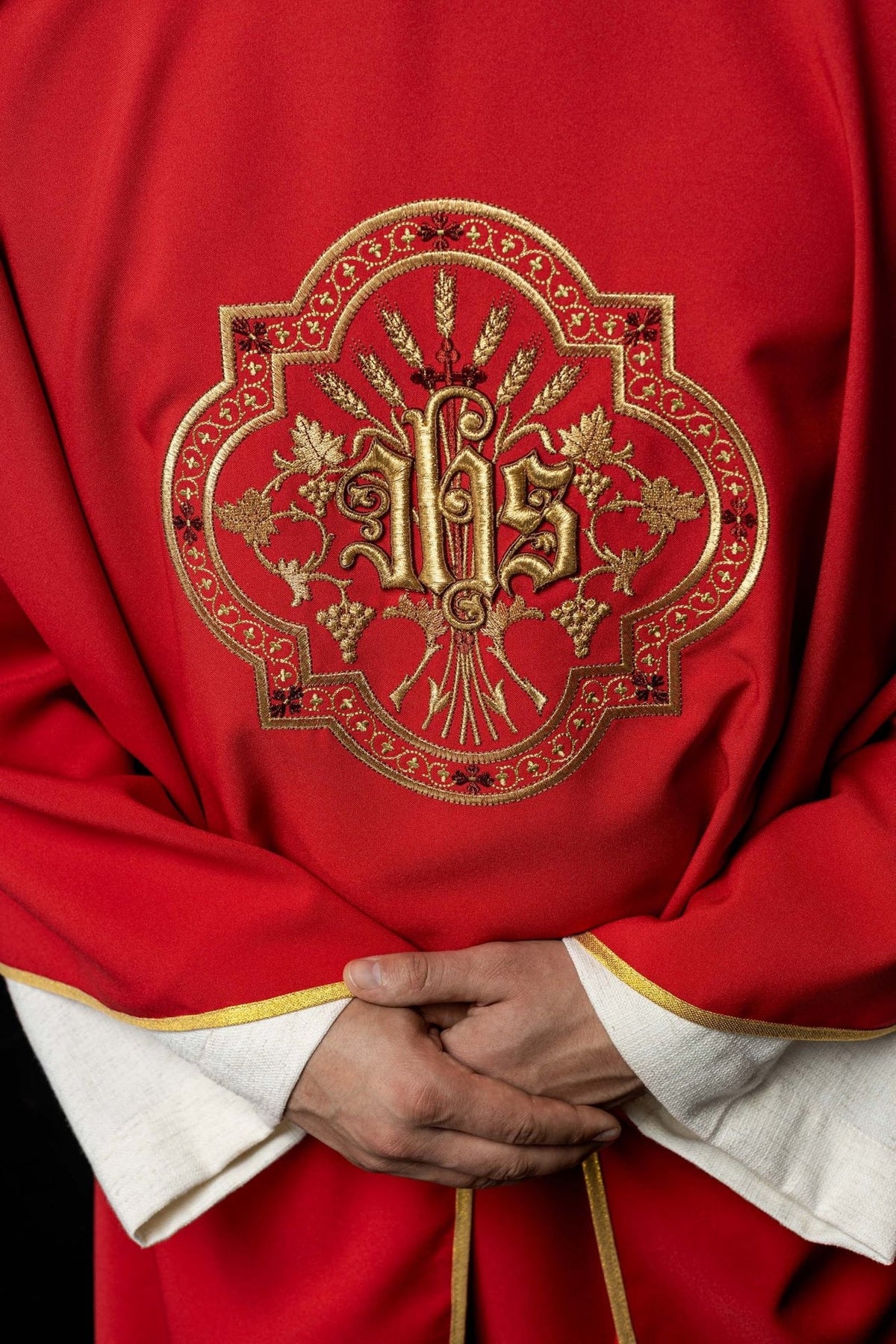 Red chasuble close-up showing gold IHS embroidery with grapes and wheat