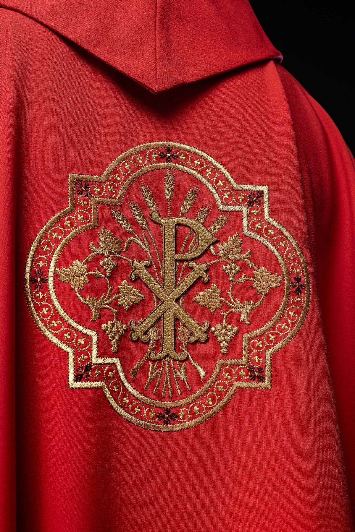 Red chasuble close-up showing gold PAX embroidery with grapes and wheat