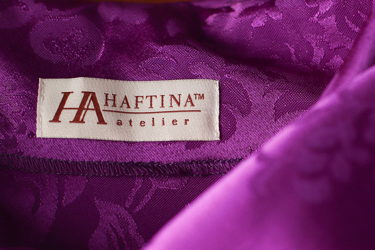 Purple chasuble fabric close-up showing jacquard pattern and sewn label